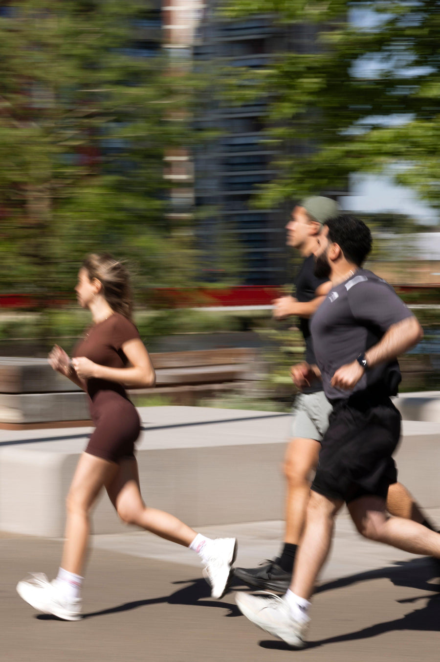 Three people running on a path with trees and buildings in the background
