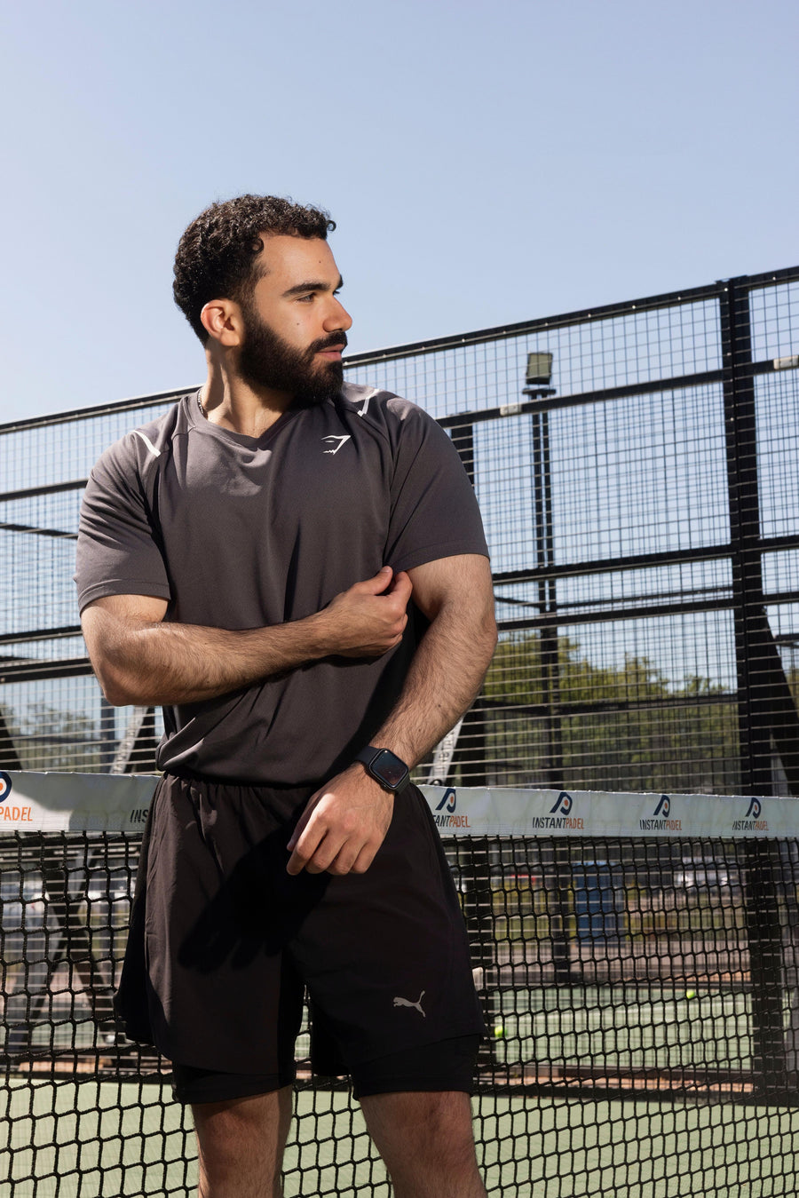 Man standing on a tennis court wearing athletic clothing with a clear sky background