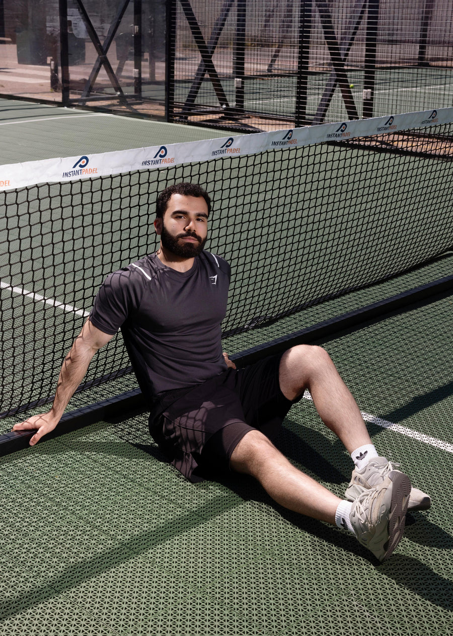 Man sitting on a tennis court next to a net with a fence in the background