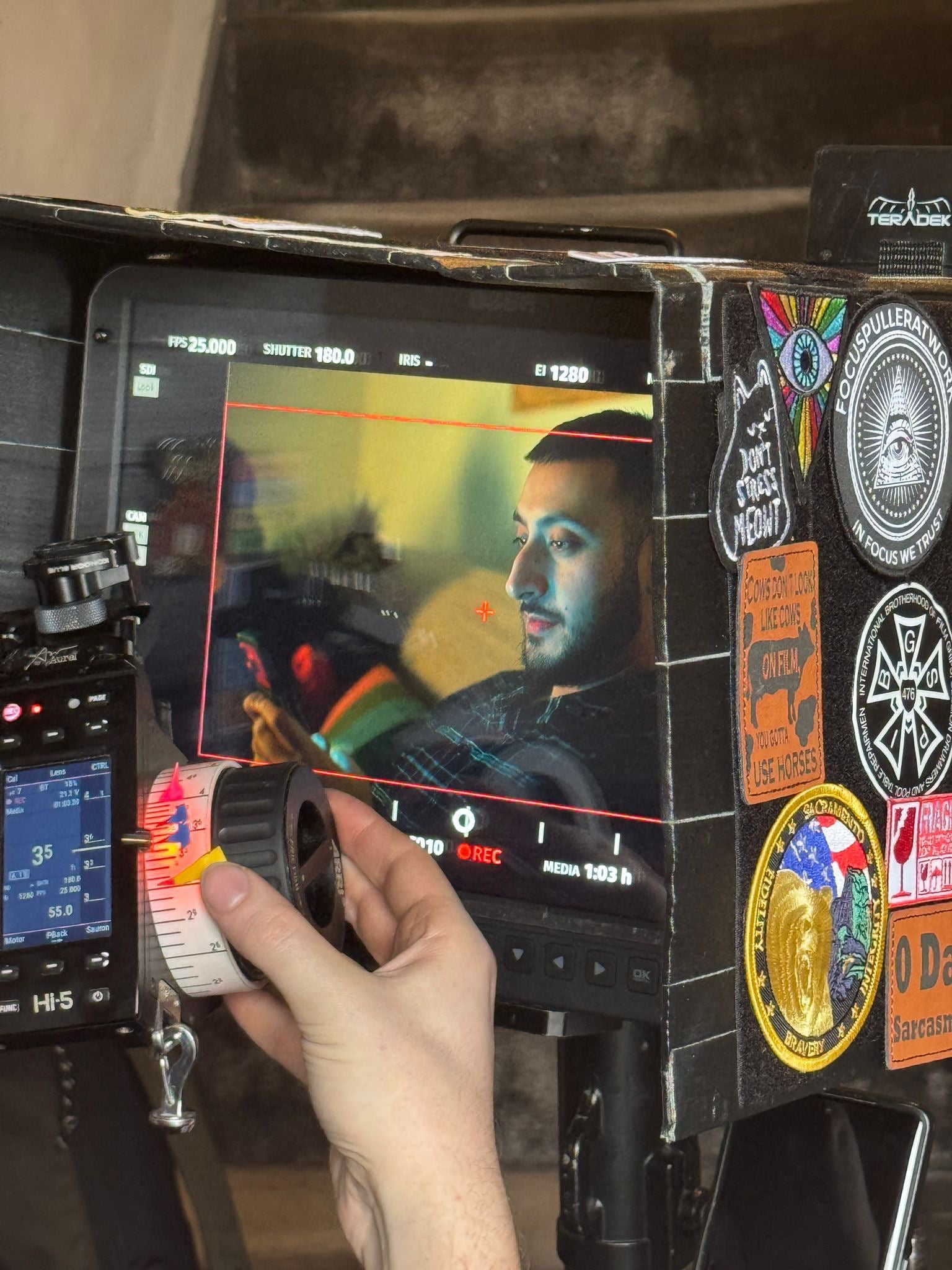 Person with a camera monitor displaying a colorful image of a man with various stickers and badges on the equipment.
