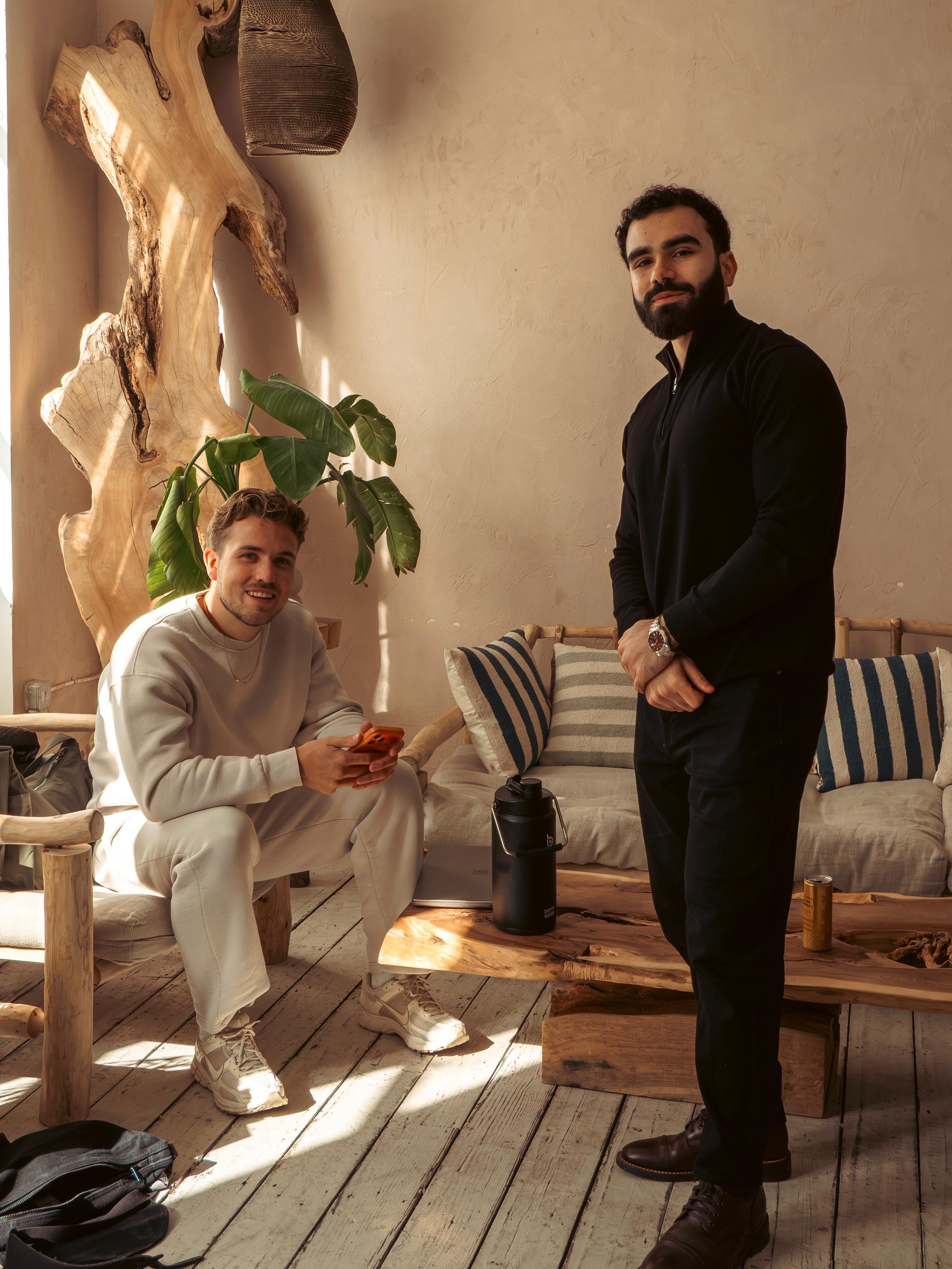 Two men in a studio with wooden furniture and plants both wearing Sonder's clothing