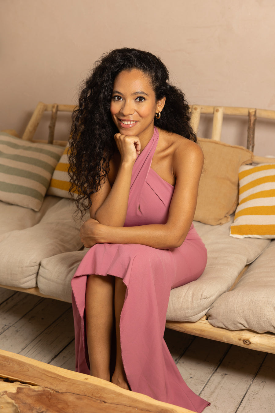 Woman in a pink dress sitting on a couch with colorful pillows.