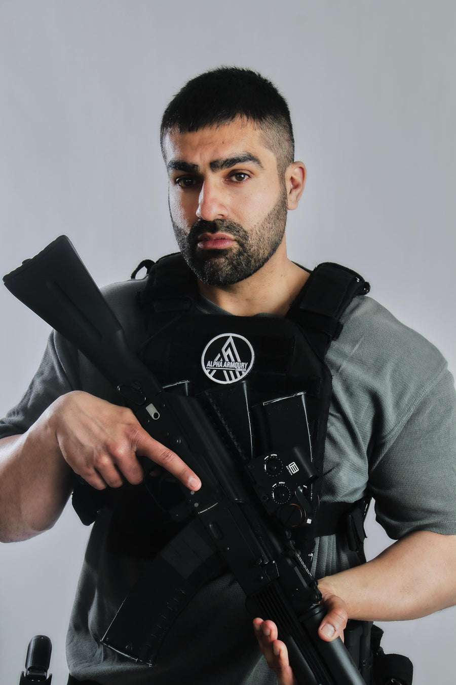 Man holding a rifle with a tactical vest against a plain background taken at our Sonder SPACT Character Profile Session.