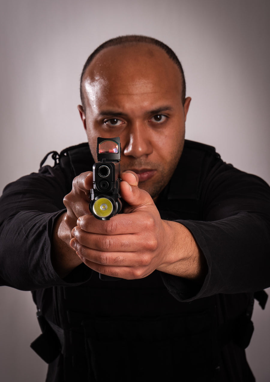 Man holding a gun towards the camera against a grey background taken at our Sonder SPACT Character Profile Session.