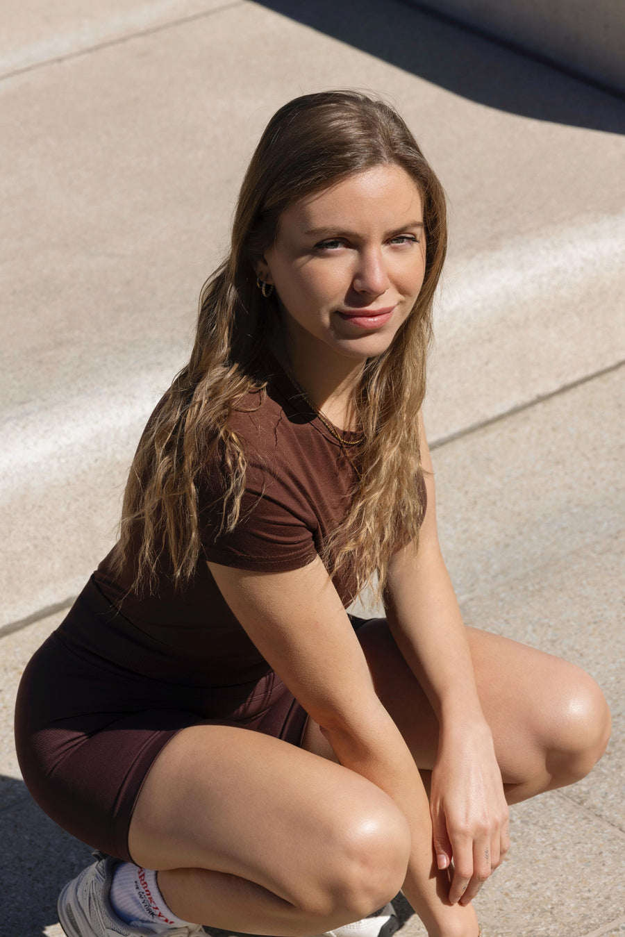 Woman sitting on a sidewalk wearing a brown outfit.