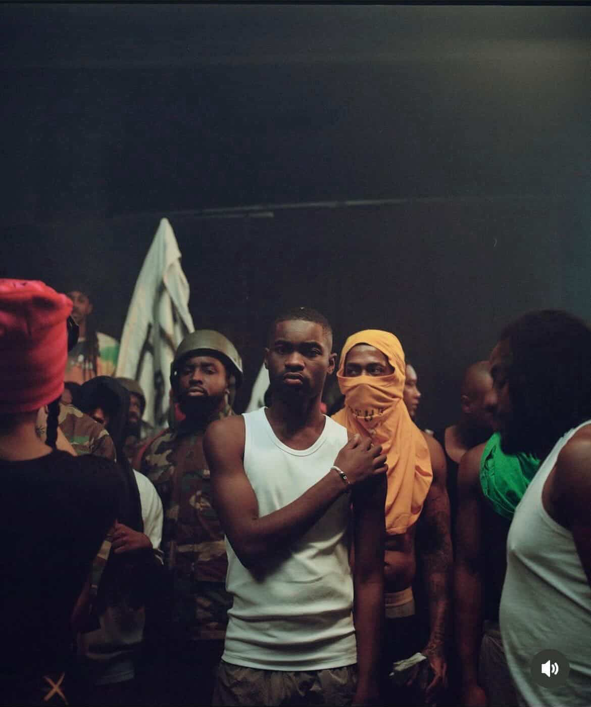Remi pictured next to British singer Dave on set for his music video. There are a group of people around them.