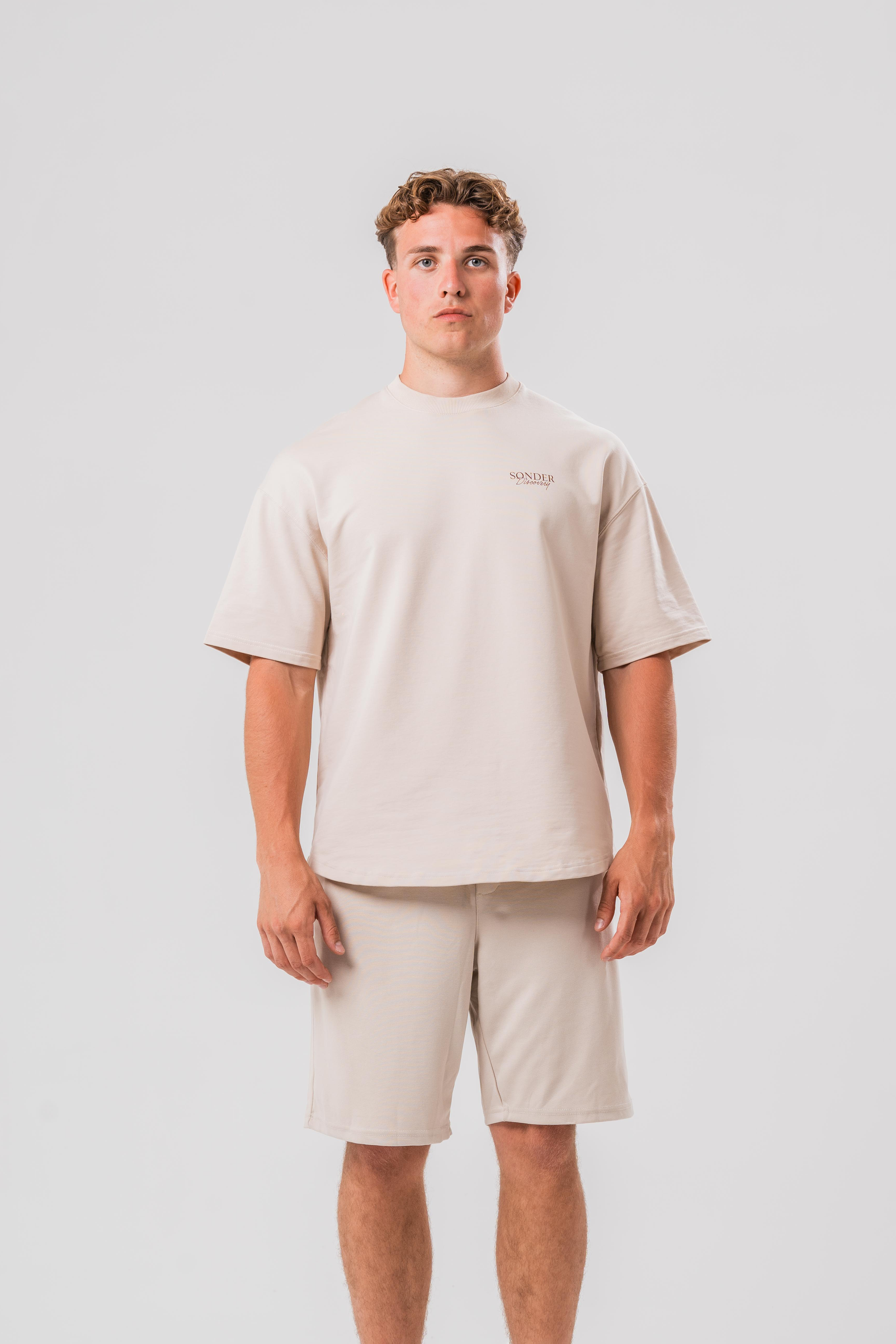 Male model wearing the Sonder Beige cowboy tee and beige shorts, in front of a light grey background