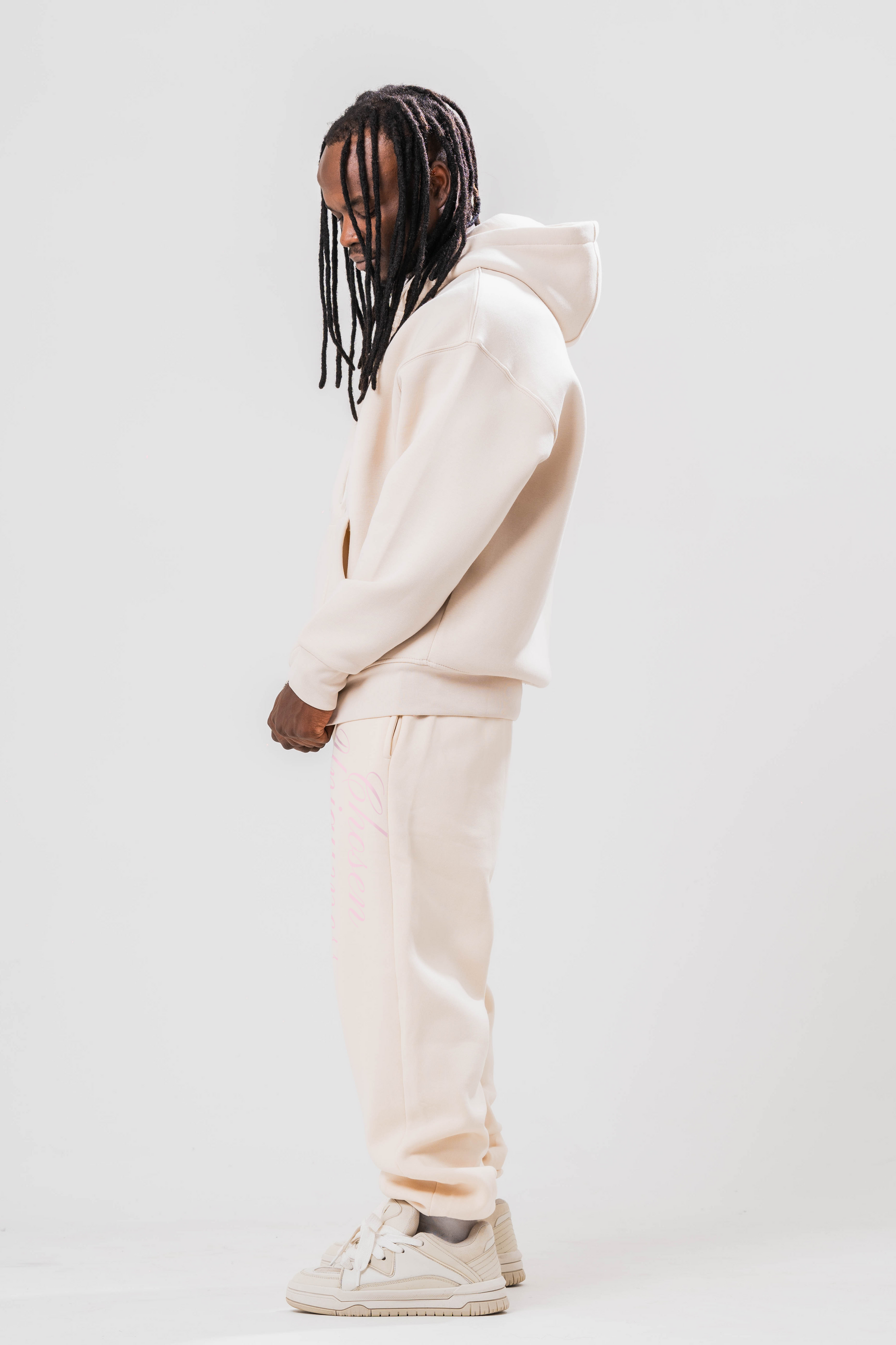 Side view of Male model wearing the Sonder Beige Oversized zip hoodie with the oversized joggers. Standing in front of a light grey background.