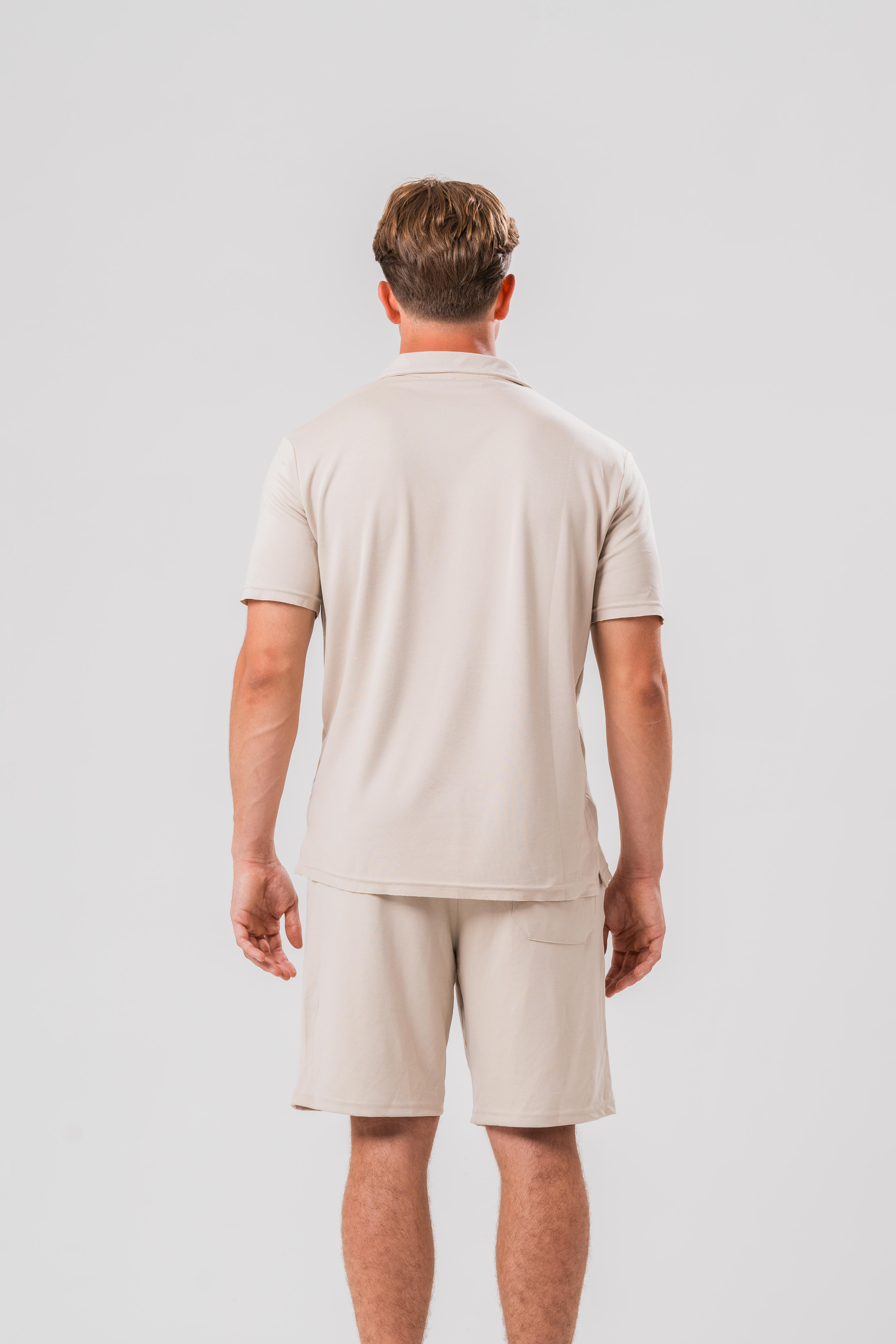 Back view of Male model wearing the Sonder Beige Summer Set including the Polo Shirt and shorts, in front of a light grey background