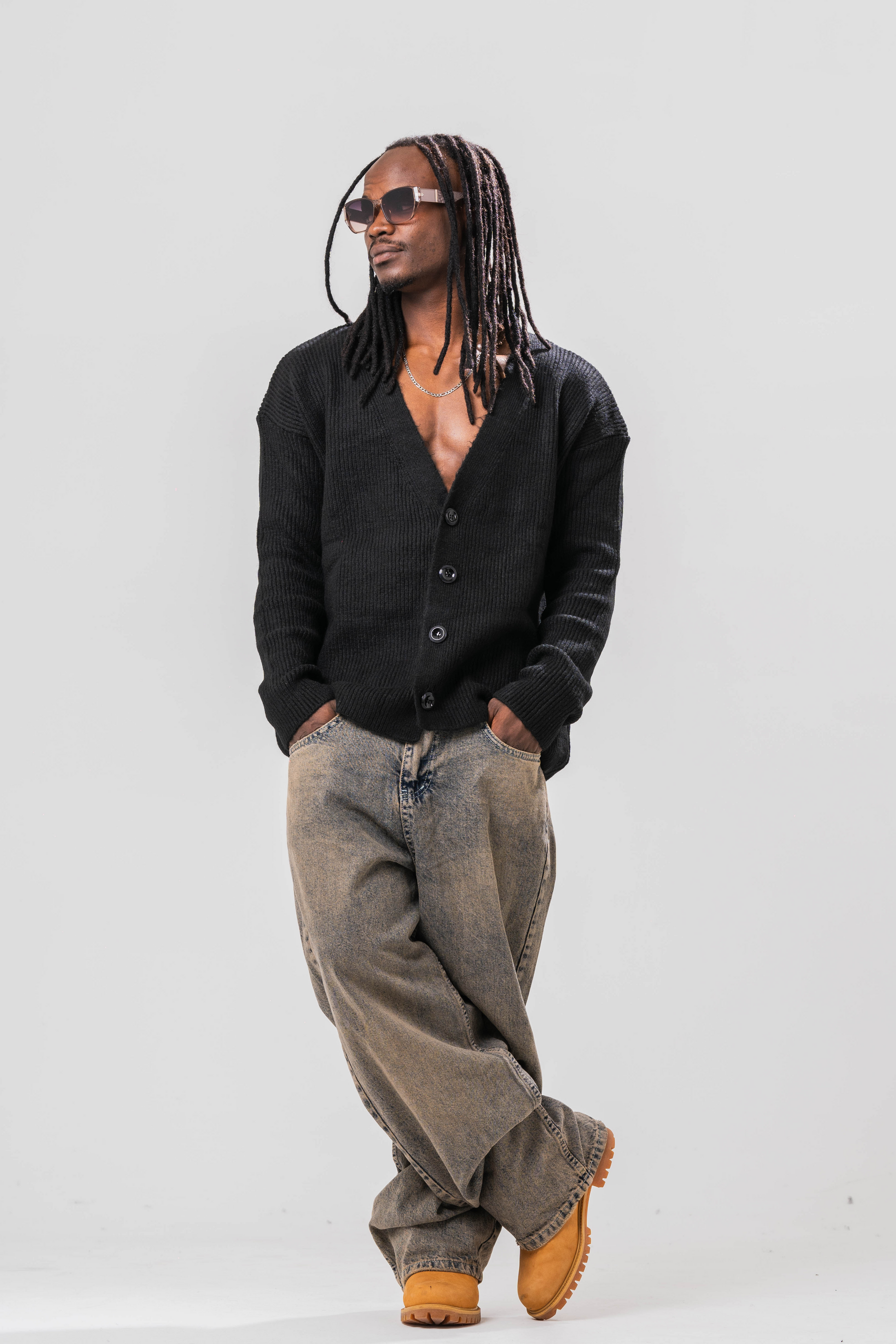 Male model wearing the Sonder Black Knit Cardigan with baggy jeans and sun glasses. In front of a light grey background.