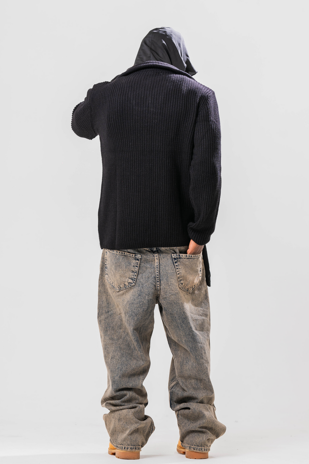 Back view of Male model wearing the Sonder Black Knit Quarter Zip with baggy jeans and a durag. In Front of a light grey background.