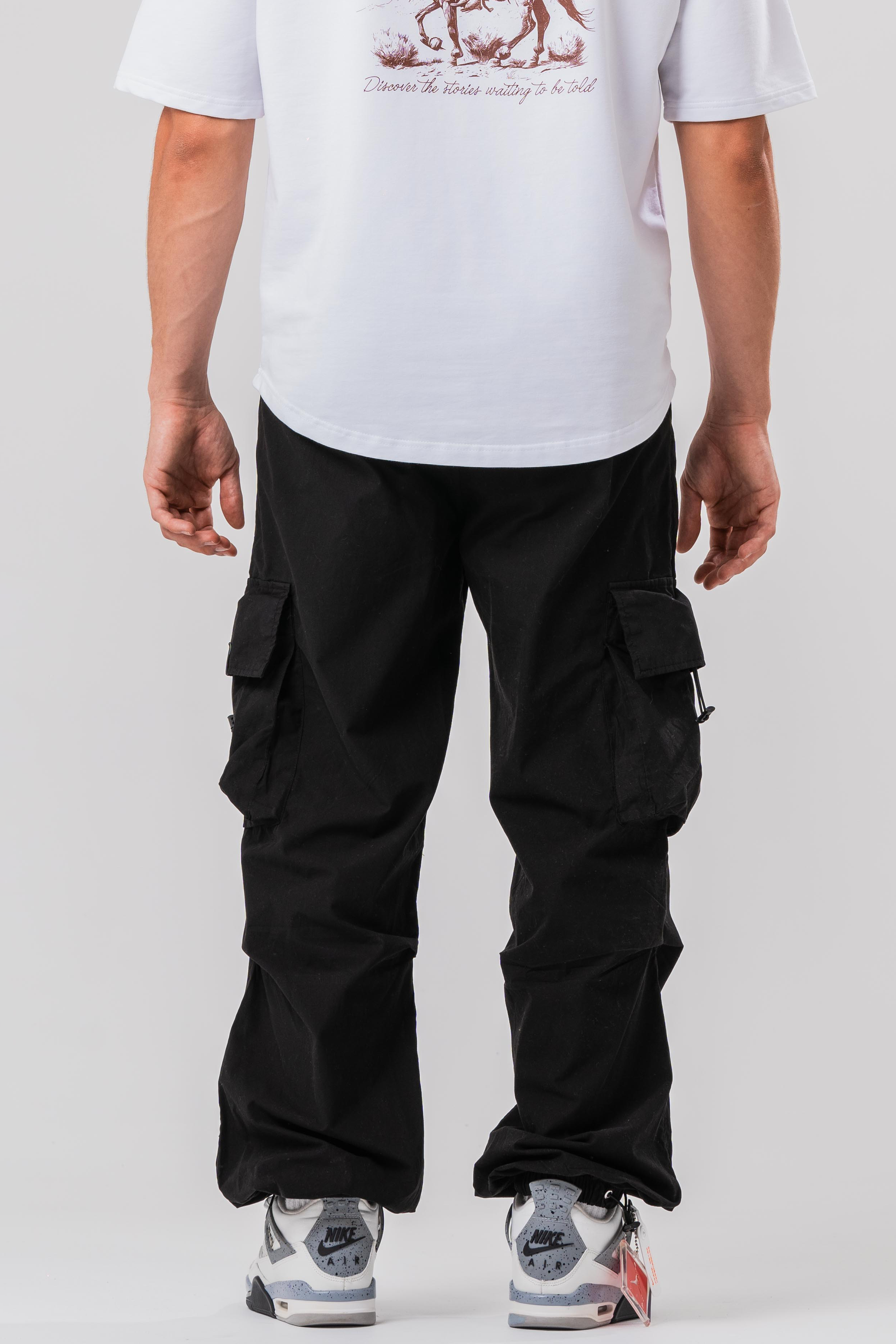 Back view of Male model wearing the Sonder Black Oversized Cargo Pants and Sonder White Oversized Graphic Cowboy T-Shirt. In front of light grey background.