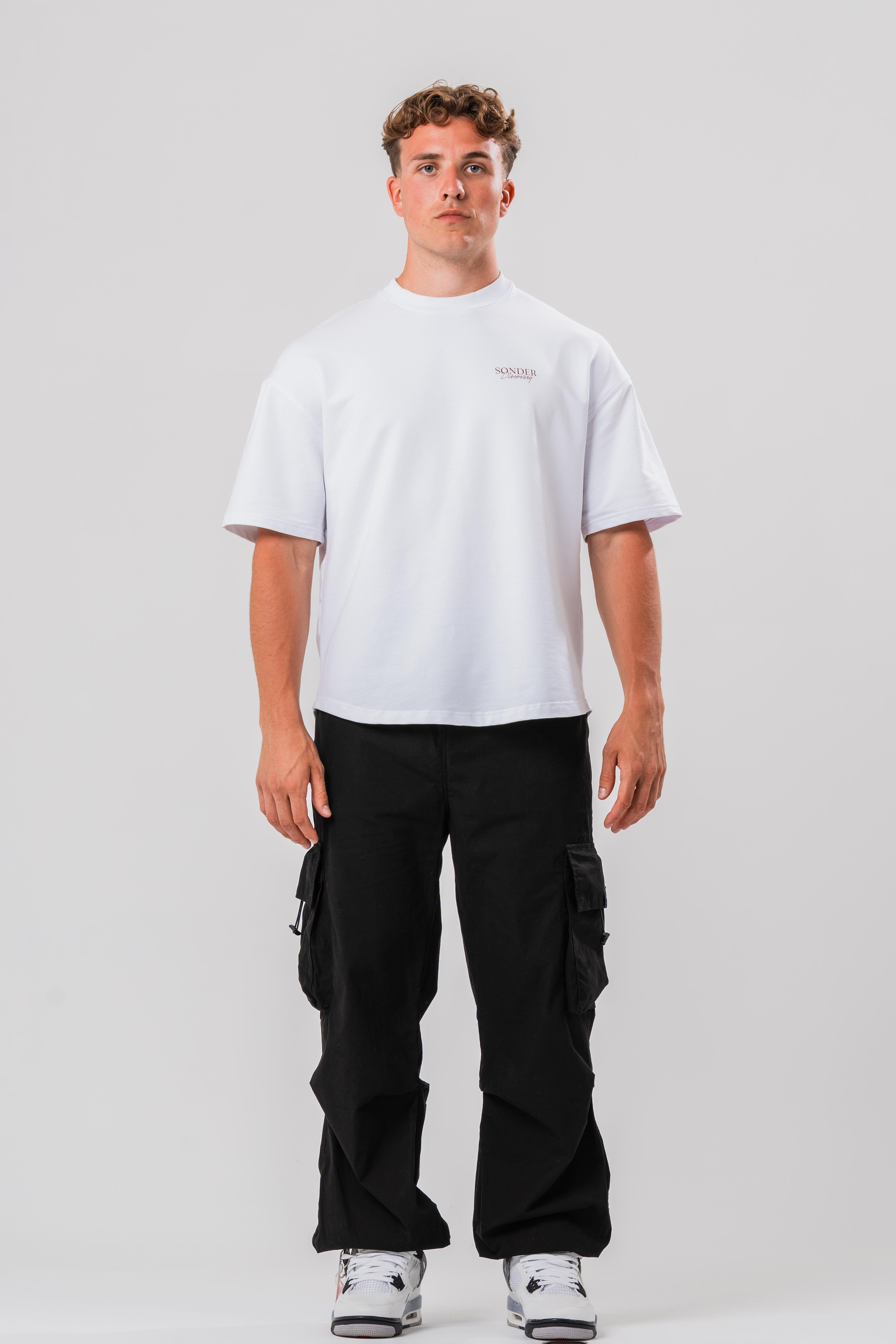 Full fit of Male model wearing the Sonder Black Oversized Cargo Pants and Sonder White Oversized Graphic Cowboy T-Shirt. In front of light grey background.
