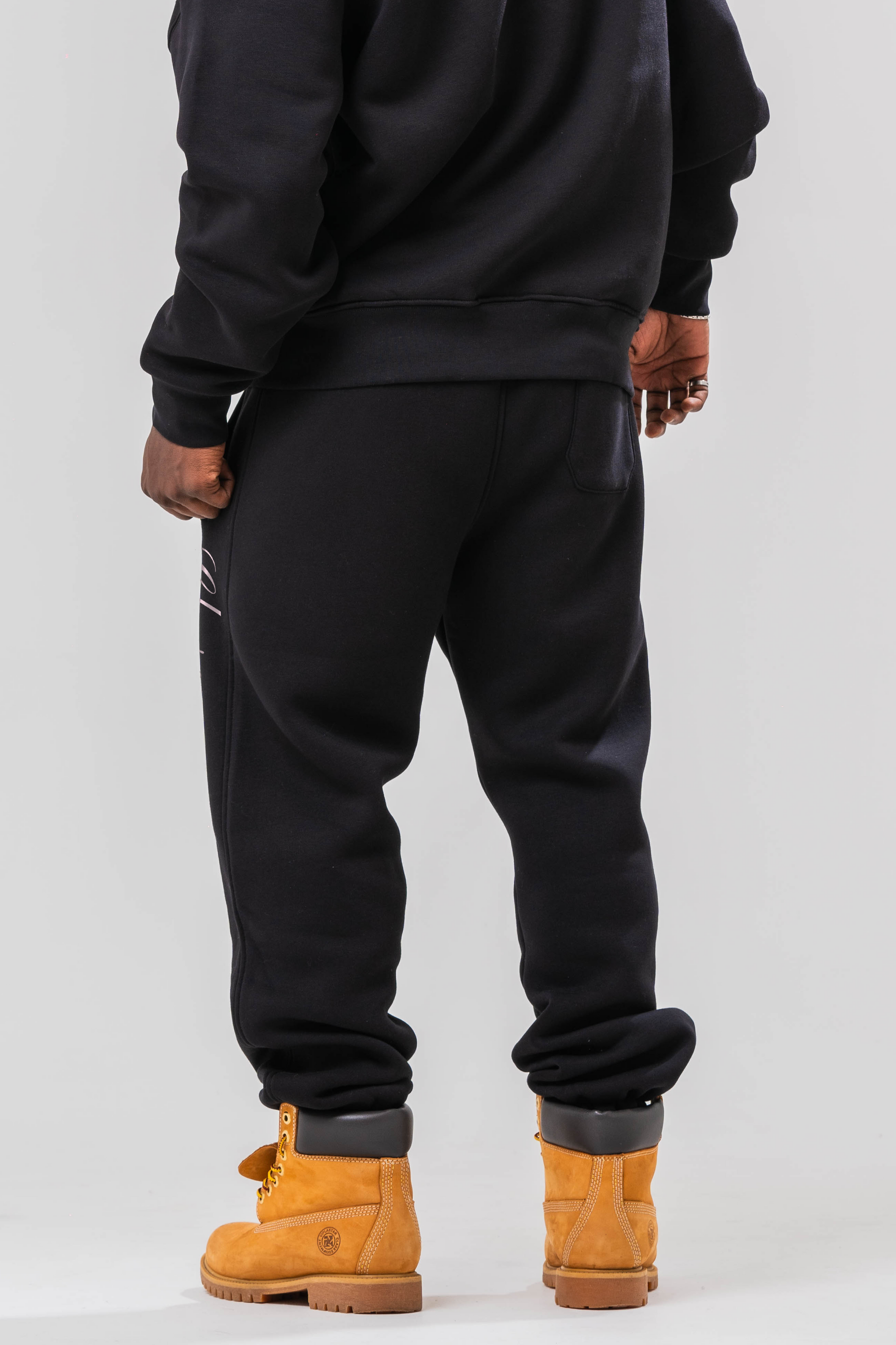 Back view of Male model wearing the Sonder Black Oversized sweatshirt with the oversized joggers. Standing in front of a light grey background.