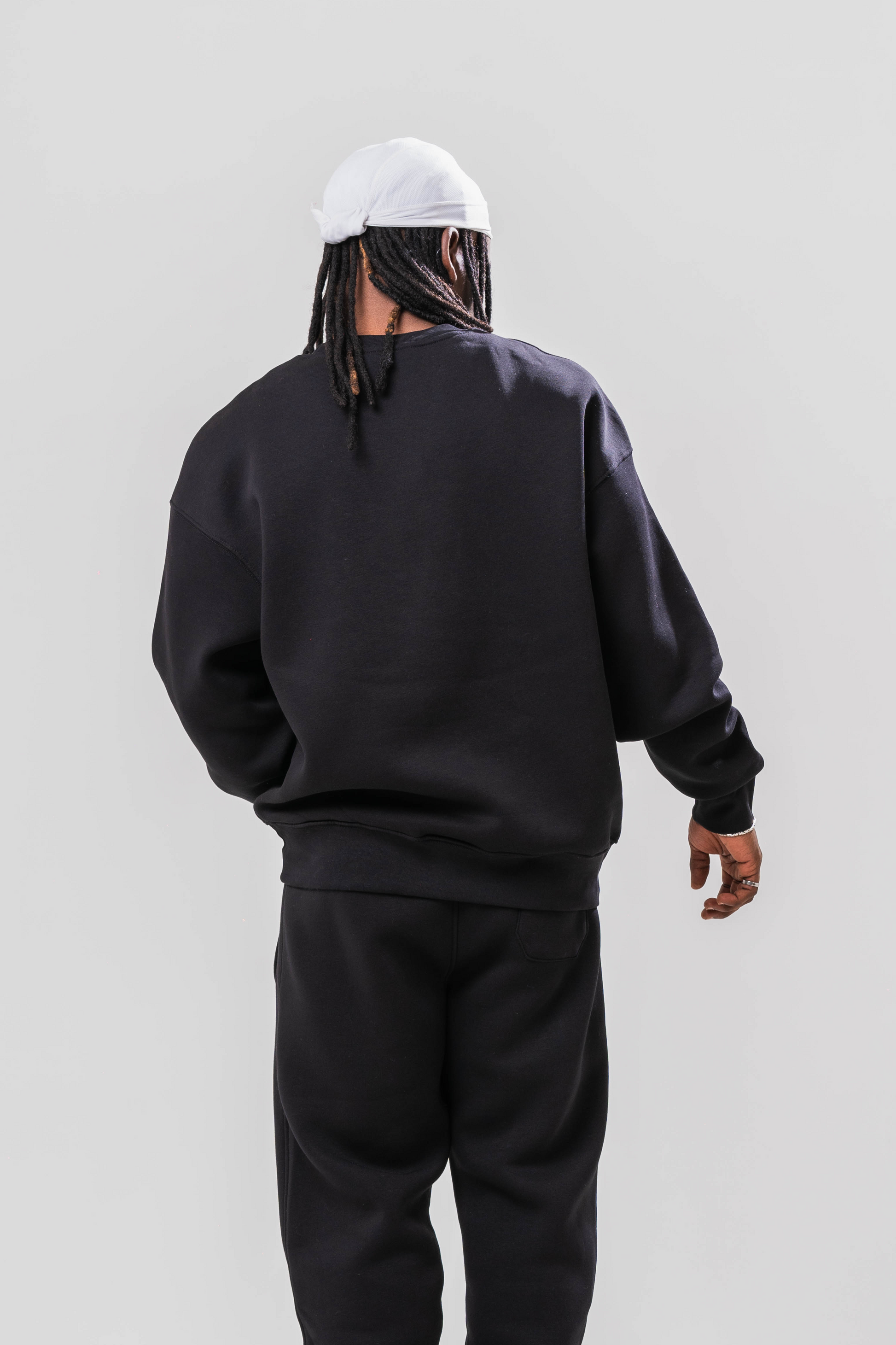 Back view of Male model wearing the Sonder Black Oversized sweatshirt with the oversized joggers. Standing in front of a light grey background.