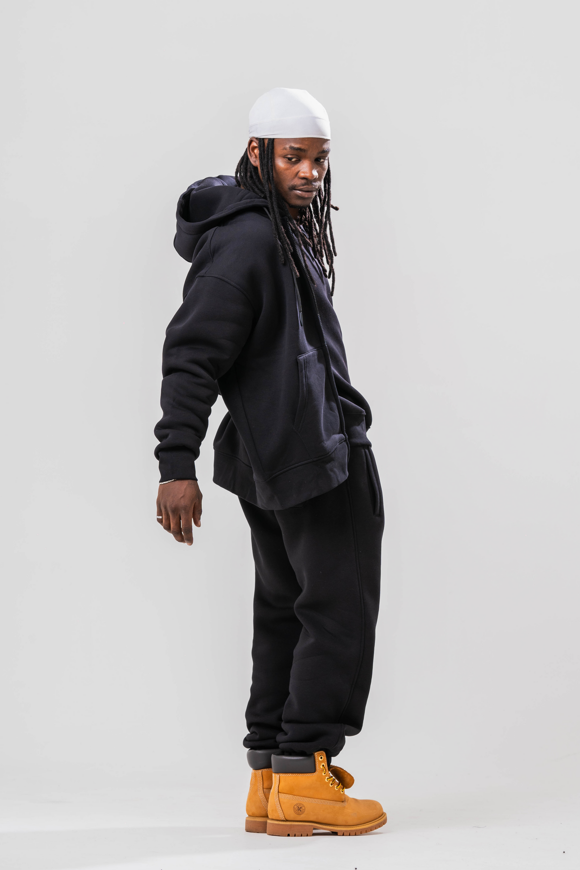 Side view of Male model wearing the Sonder Black Oversized zip hoodie with the oversized joggers and black tee. Standing in front of a light grey background.
