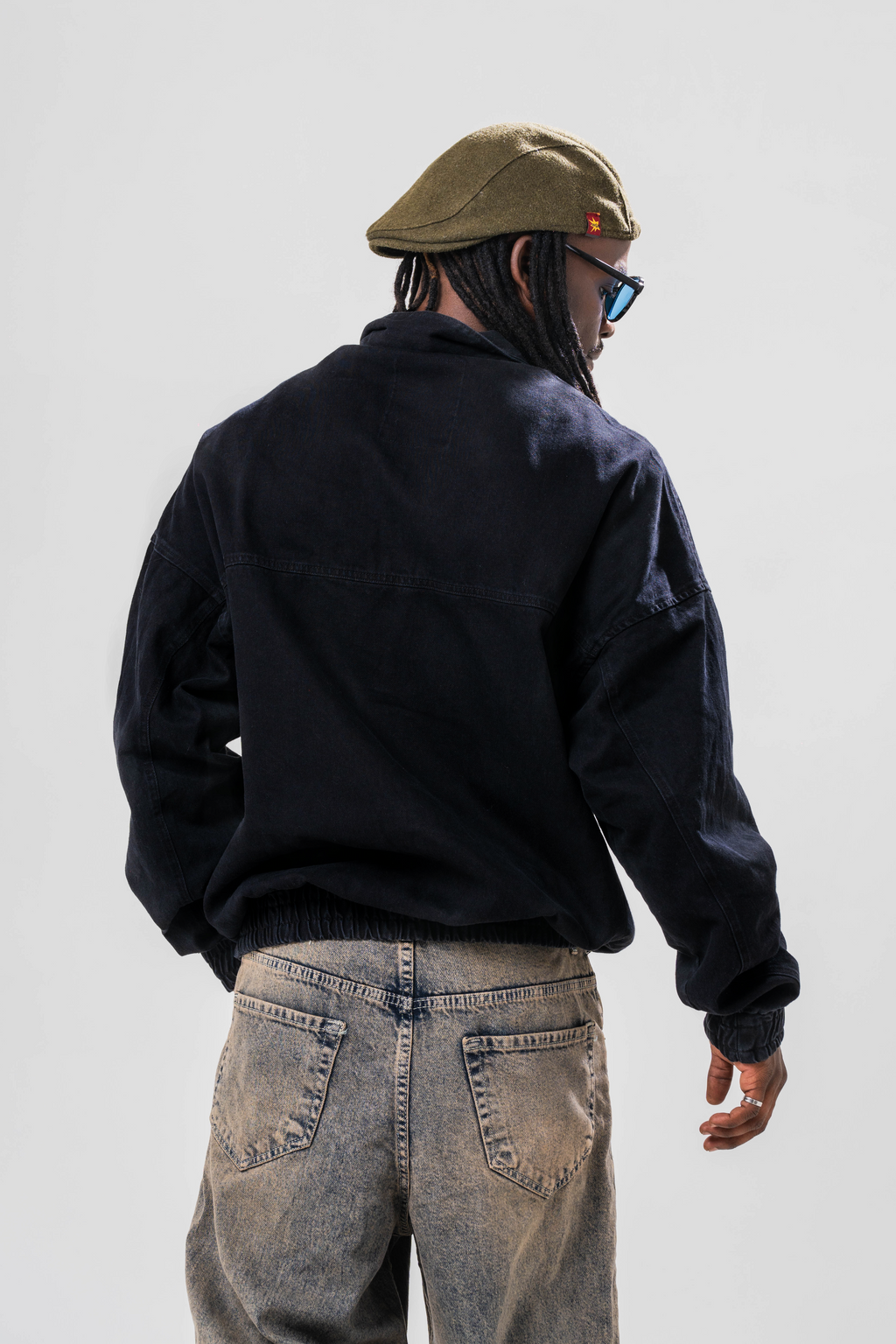 Back view of Male model wearing the Sonder Black Quarter zip pullover part of our AP collection, with jeans and a hat in front of light grey background.