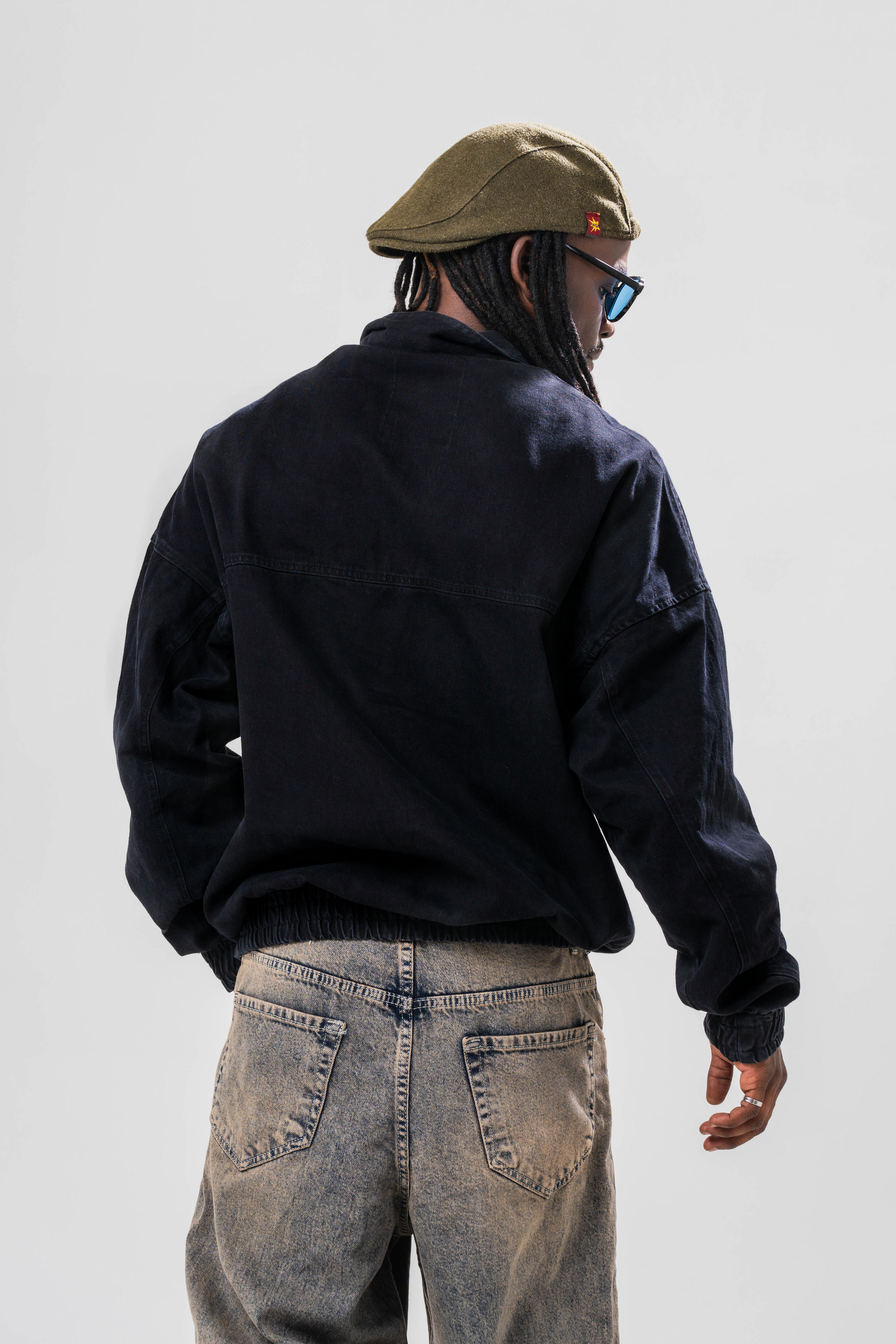 Back view of Male model wearing the Sonder Black Quarter zip pullover part of our AP collection, with jeans and a hat in front of light grey background.