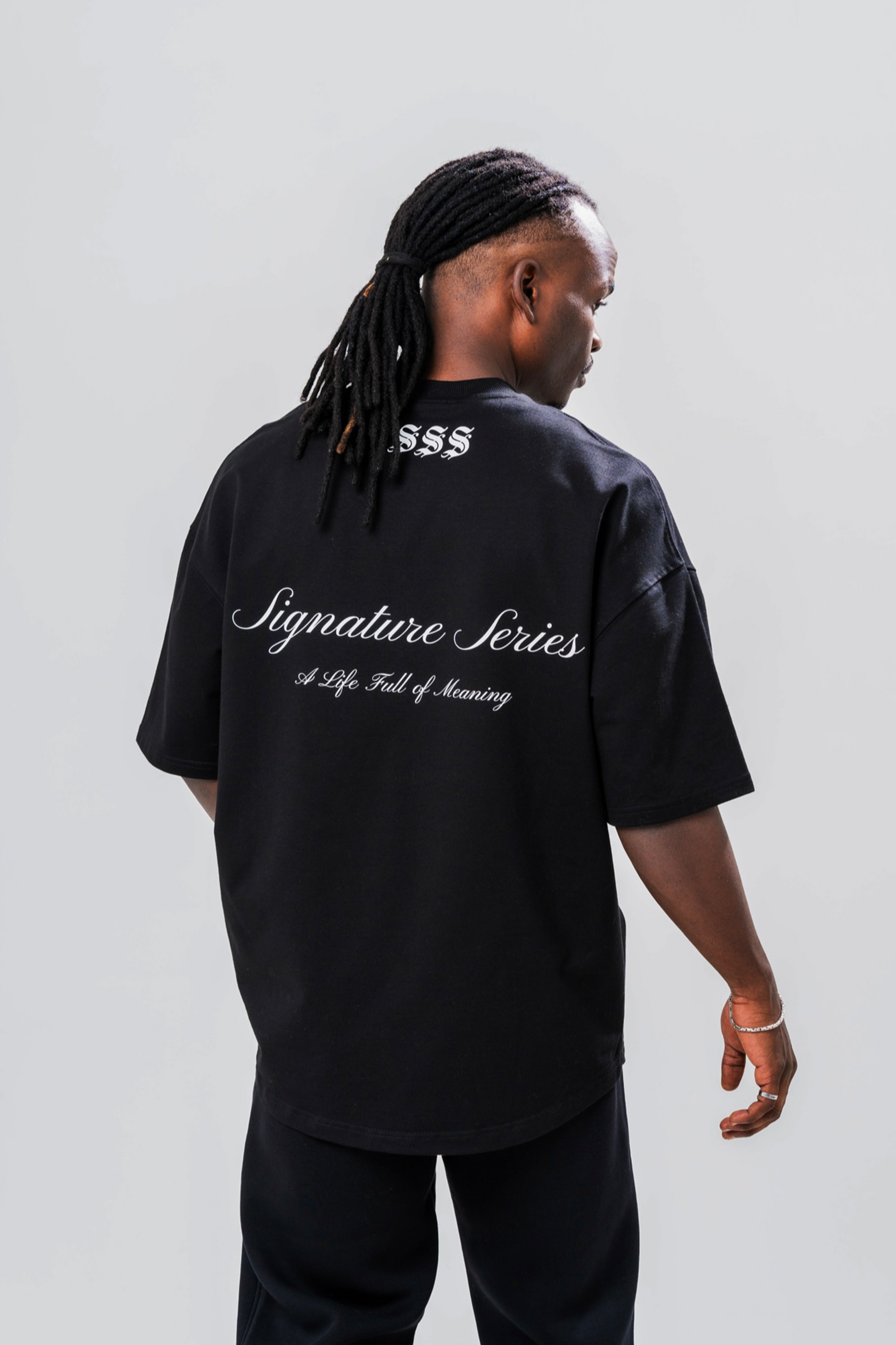 Back view of Male model wearing the Sonder Signature Series Black oversized t-shirt and black joggers, in front of a light grey background