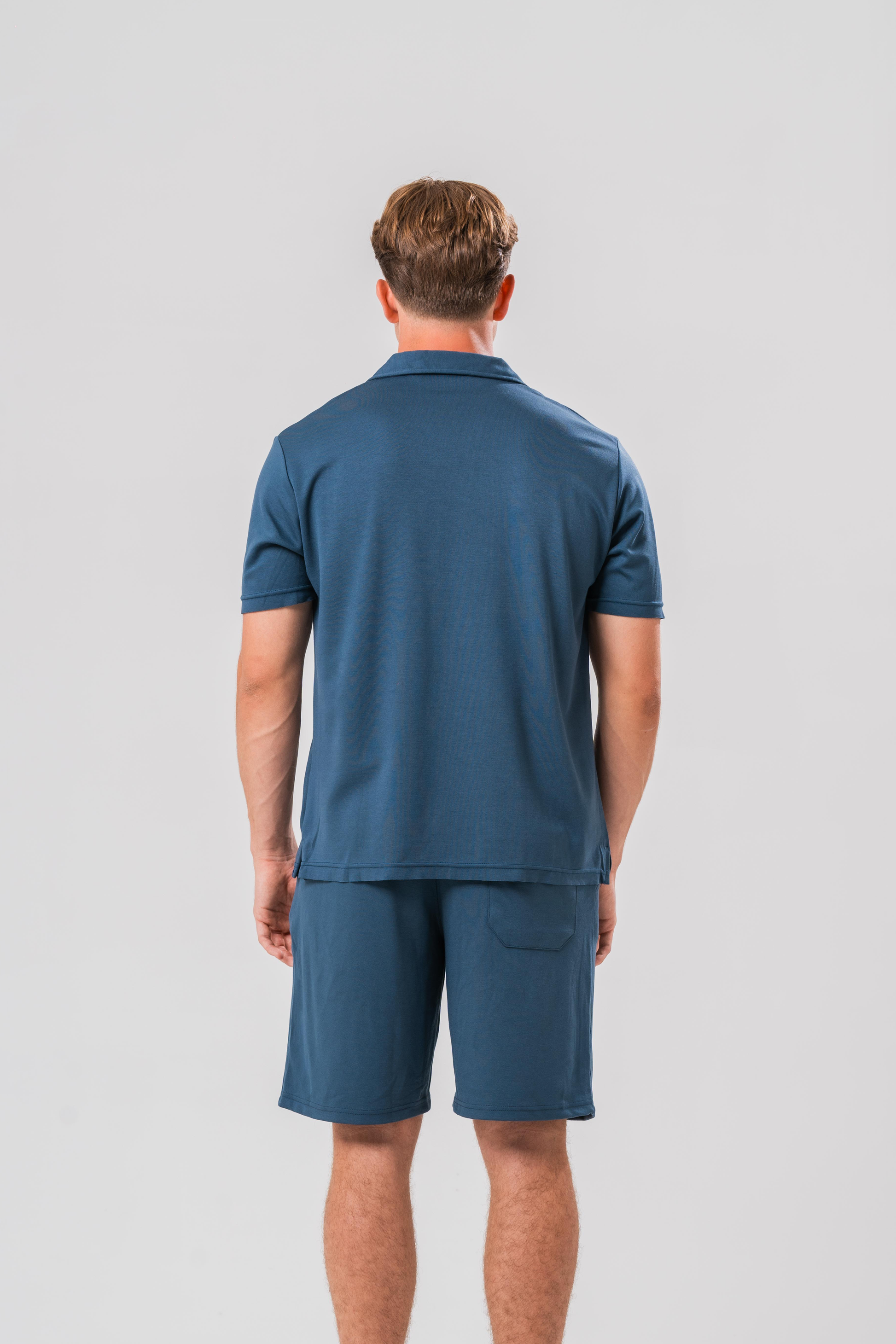 Back view of Male model wearing the Sonder Blue Cotton Set including the Polo Shirt and shorts, in front of a light grey background