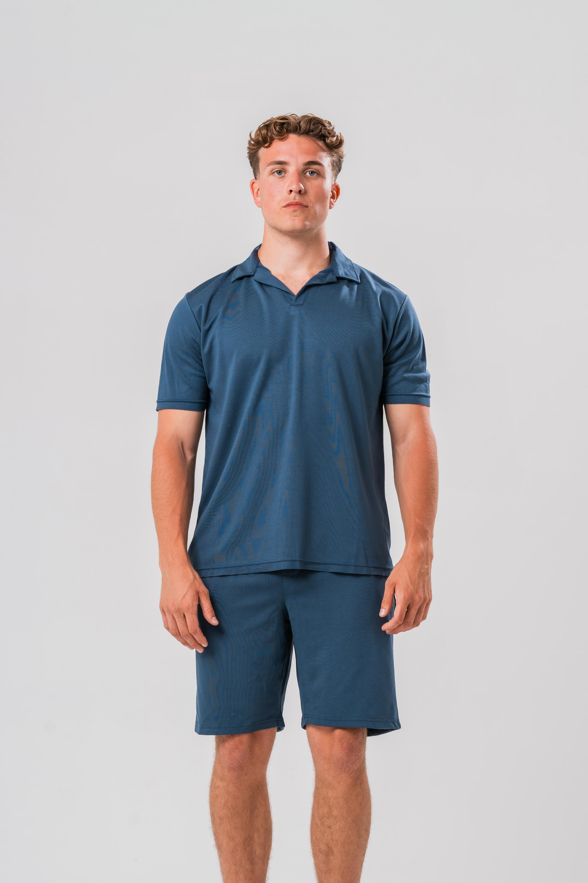 Male model wearing the Sonder Blue Cotton Set including the Polo Shirt and shorts, in front of a light grey background