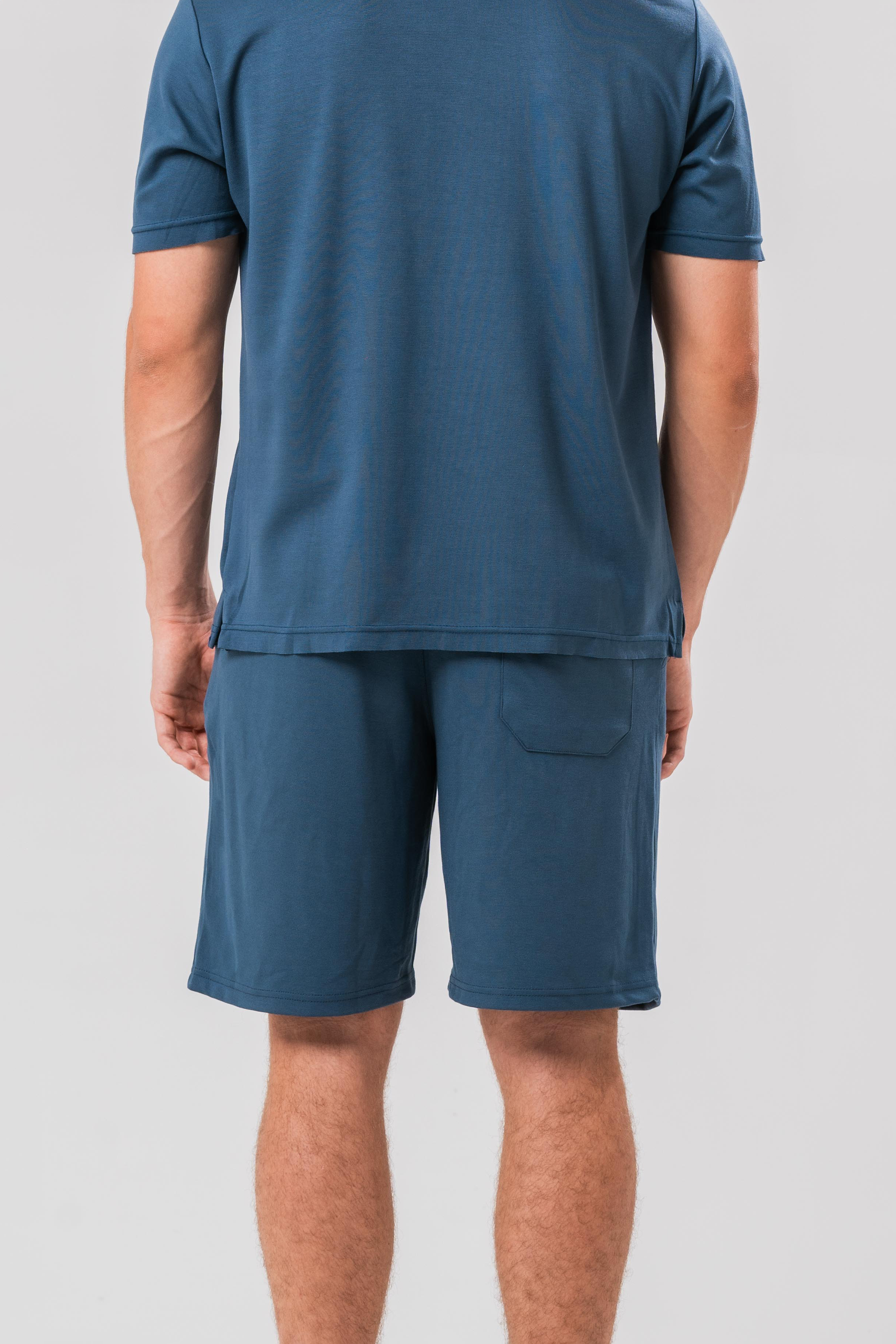 Back view of Male model wearing the Sonder Blue Cotton Set including the Polo Shirt and shorts, in front of a light grey background