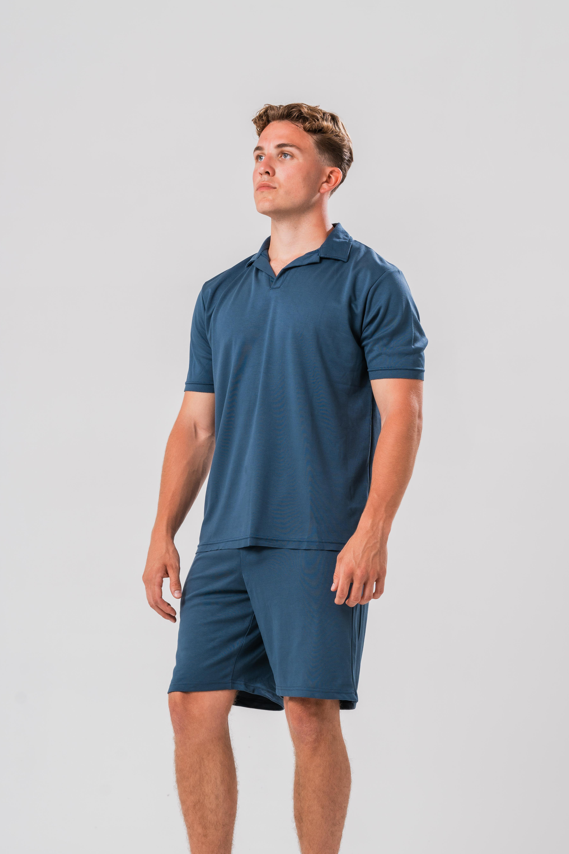 Side view Male model wearing the Sonder Blue Cotton Set including the Polo Shirt and shorts, in front of a light grey background
