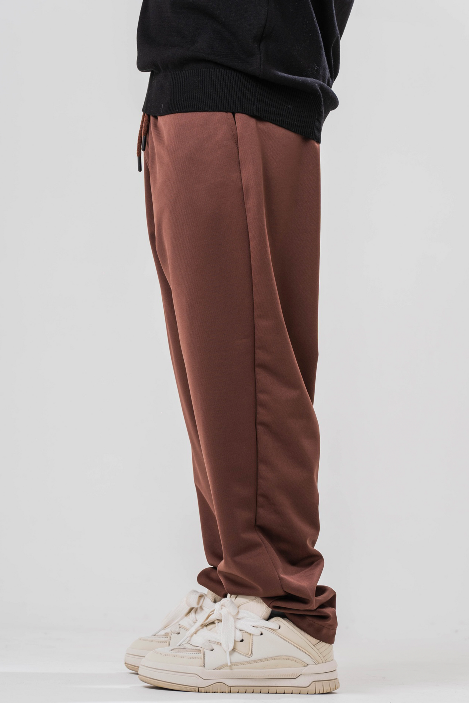 Side view of Male model wearing the Sonder Brown Relaxed Sweatpants and the black quarter zip. Standing in front of a light grey background.