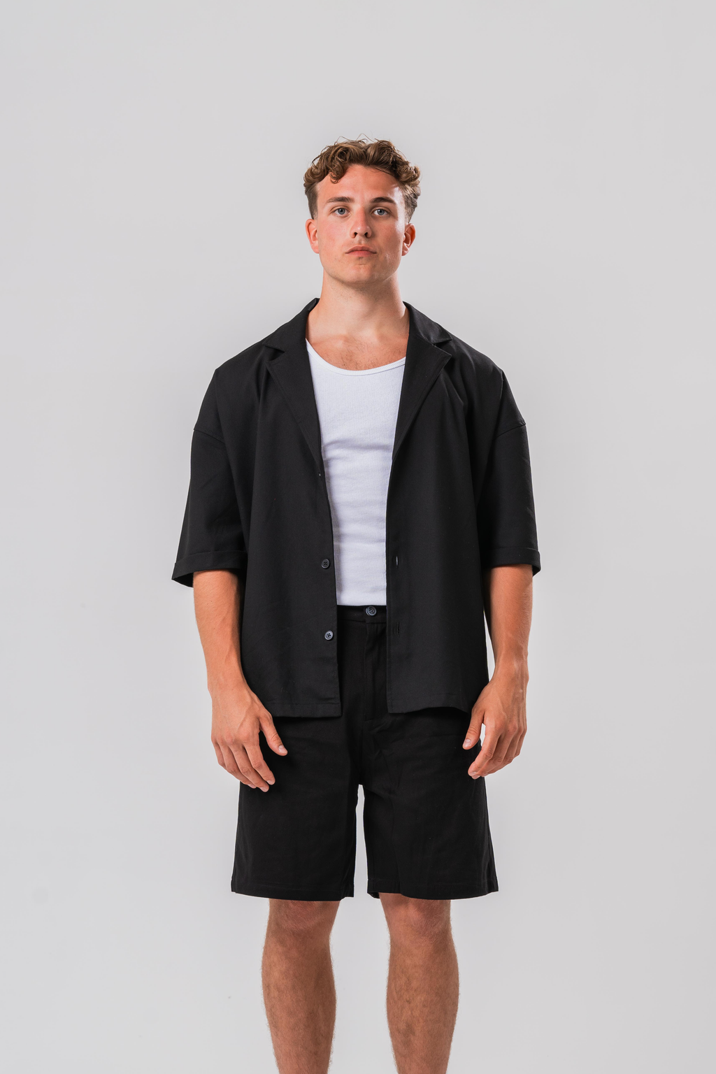 Male model wearing a white under layer with the Sonder Classic Black oversized shirt and shorts, in front of a light grey background