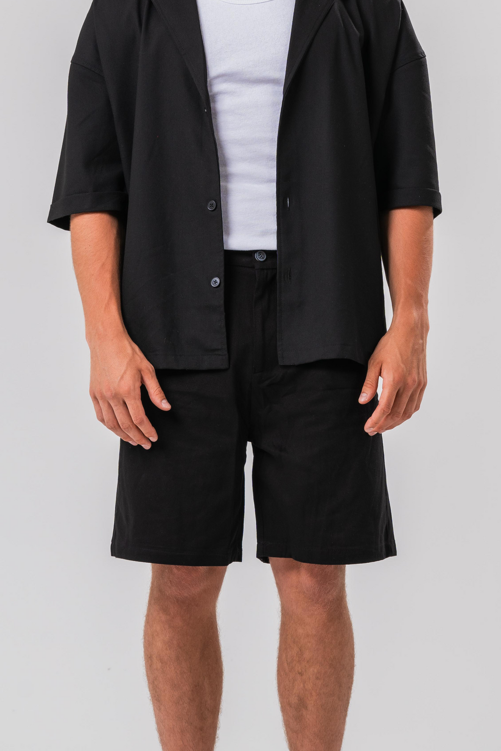 Close up view of Male model wearing a white under layer with the Sonder Classic Black oversized shirt and shorts, in front of a light grey background