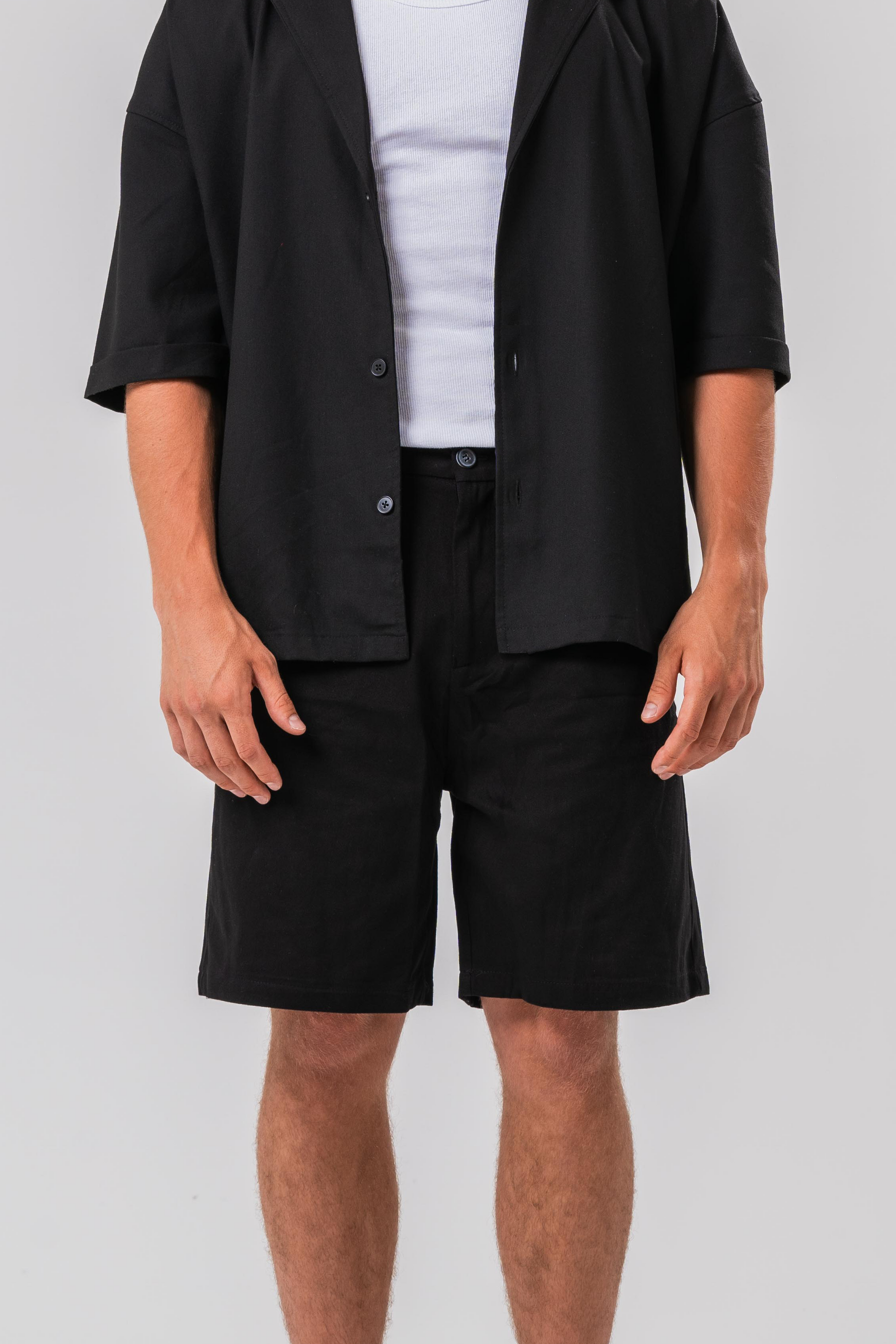 Close up view of Male model wearing a white under layer with the Sonder Classic Black oversized shirt and shorts, in front of a light grey background