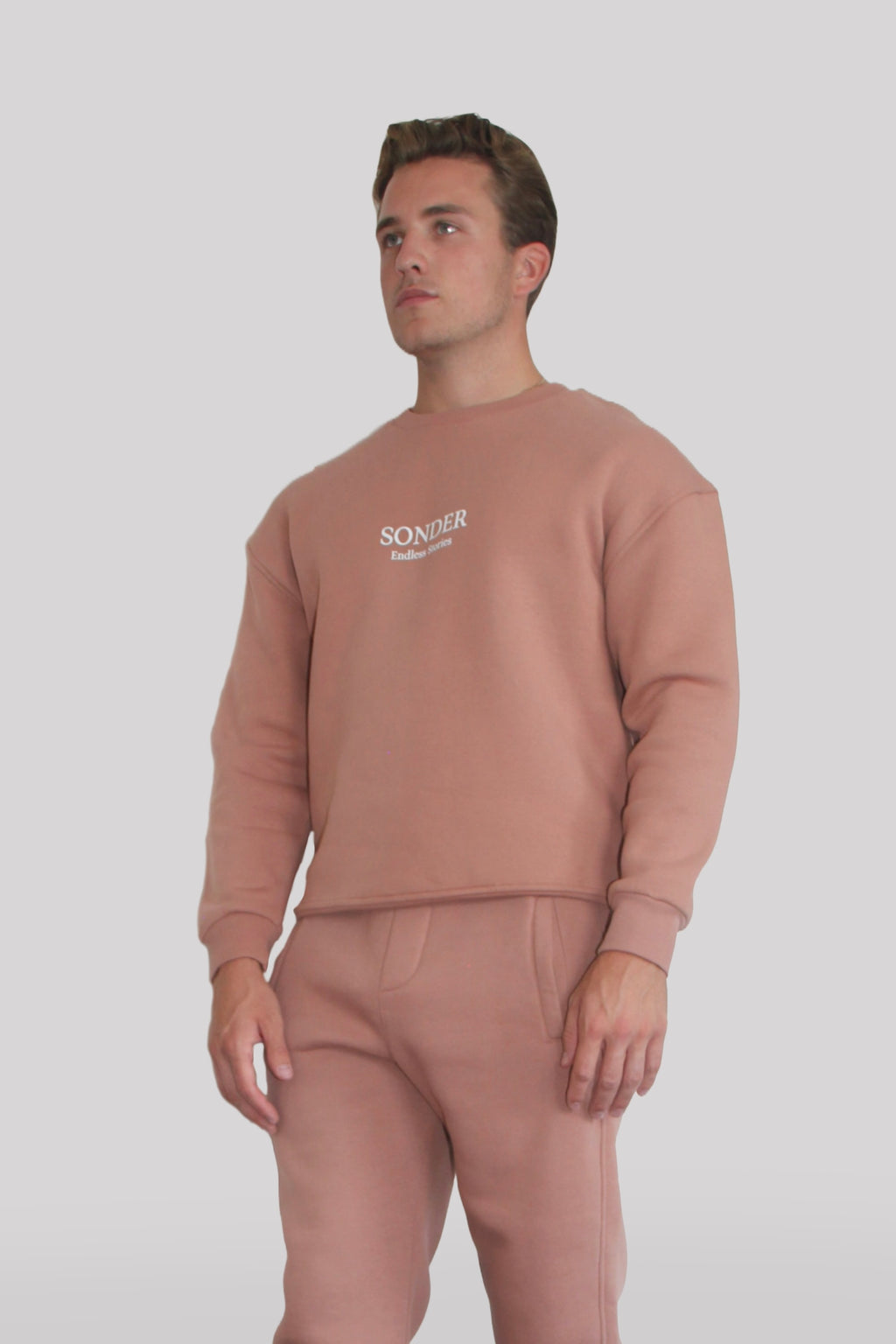 Side view of Male model wearing the Sonder Copper Signature Series Sweatshirt with SONDER branding paired with the Copper Signature Series Sweatpants. In front of a light grey background