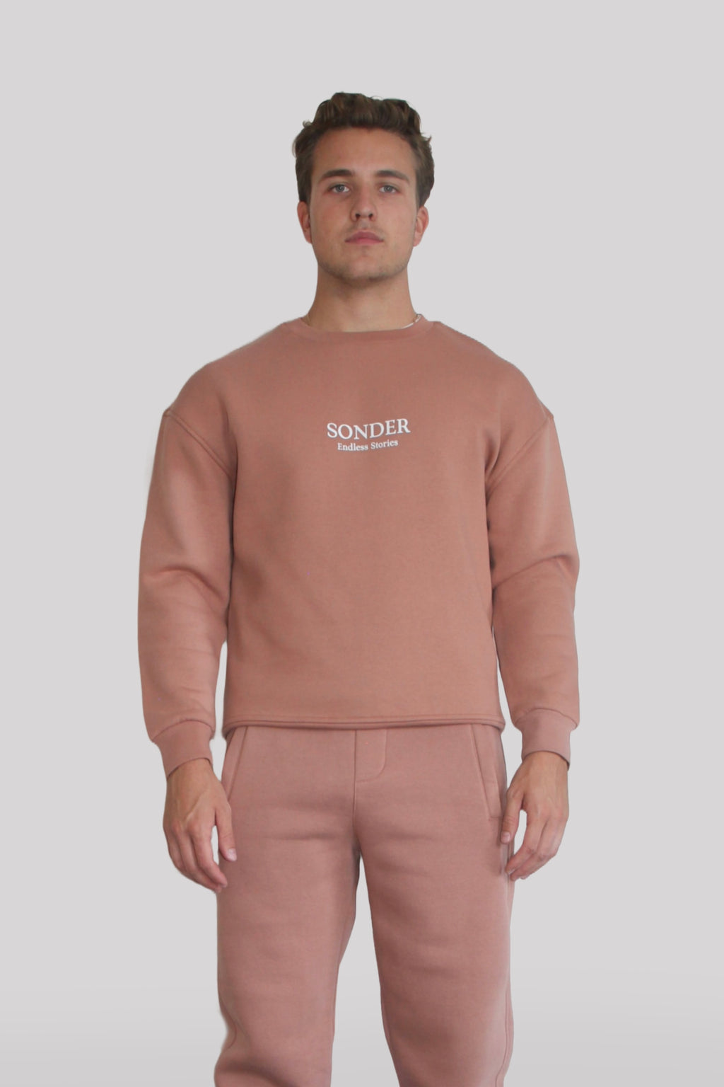 Male model wearing the Sonder Copper Signature Series Sweatshirt with SONDER branding paired with the Copper Signature Series Sweatpants. In front of a light grey background