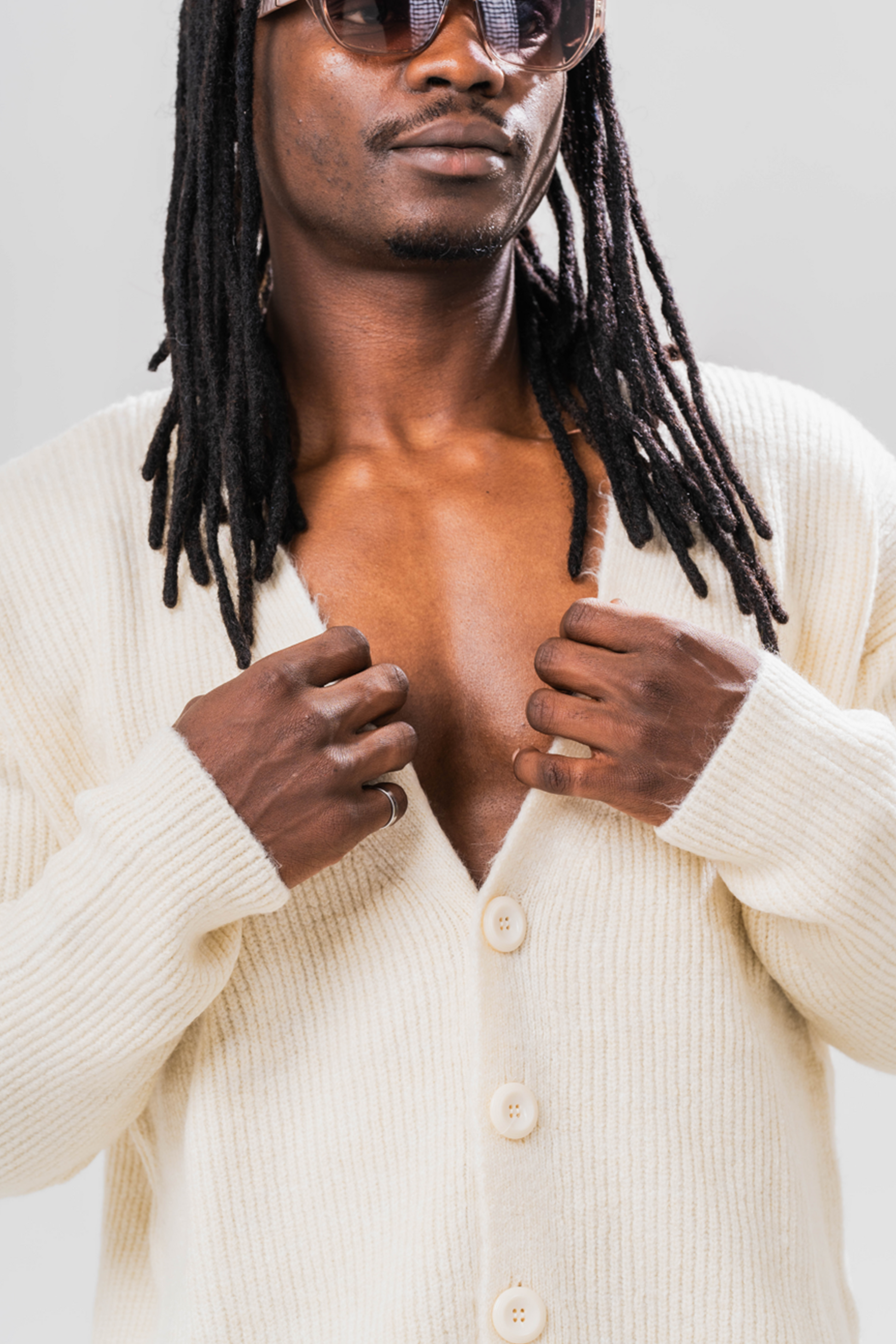 Close up of Male model wearing the Sonder Cream Knit Cardigan with sun glasses. In front of a light grey background.