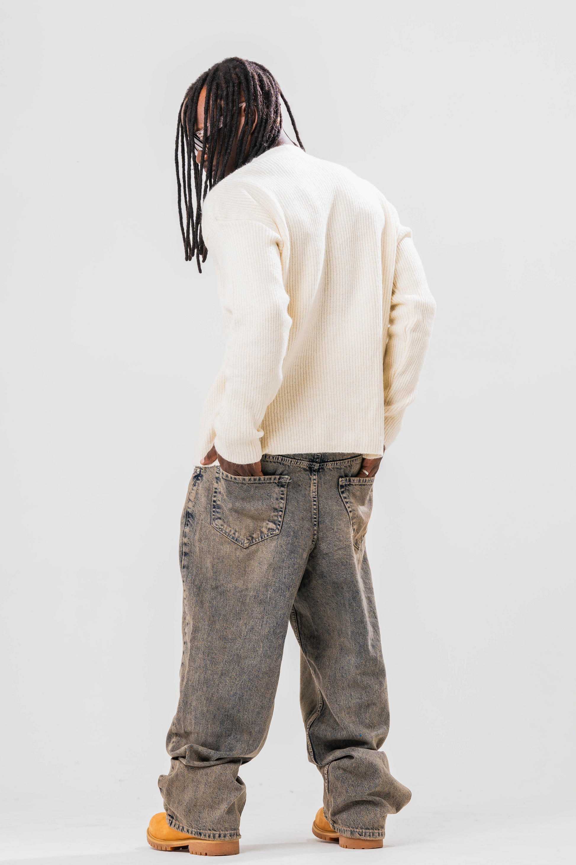 Back view of Male model wearing Sonder cream knit cardigan and baggy jeans. On a light grey background