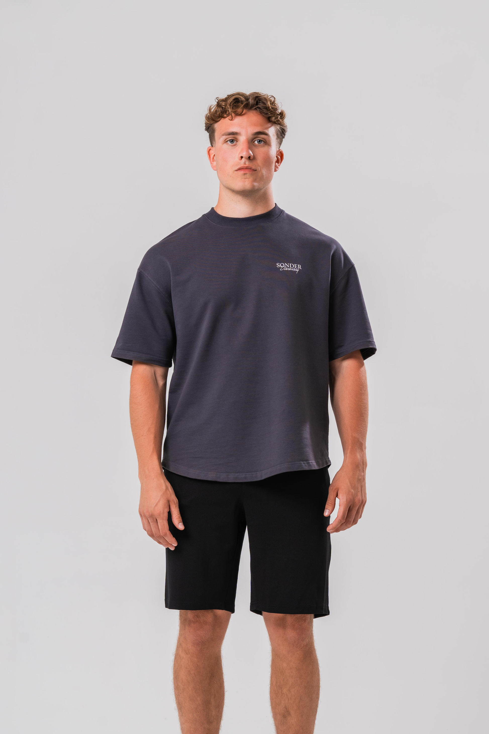 Male model wearing the Sonder Grey cowboy T-shirt and black shorts, in front of a light grey background 
