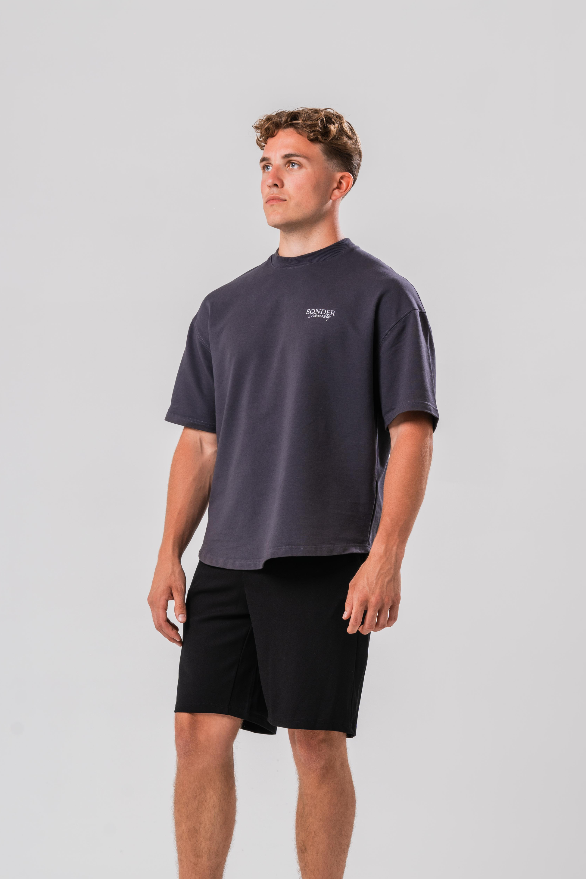 Side View of Male model wearing the Sonder Grey cowboy T-shirt and black shorts, in front of a light grey background