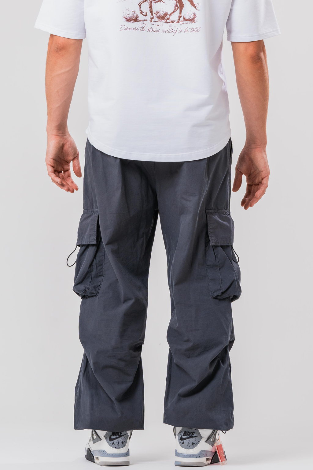 Back view of Male model wearing the Sonder Grey Oversized Cargo Pants and Sonder White Oversized Graphic Cowboy T-Shirt. In front of light grey background.