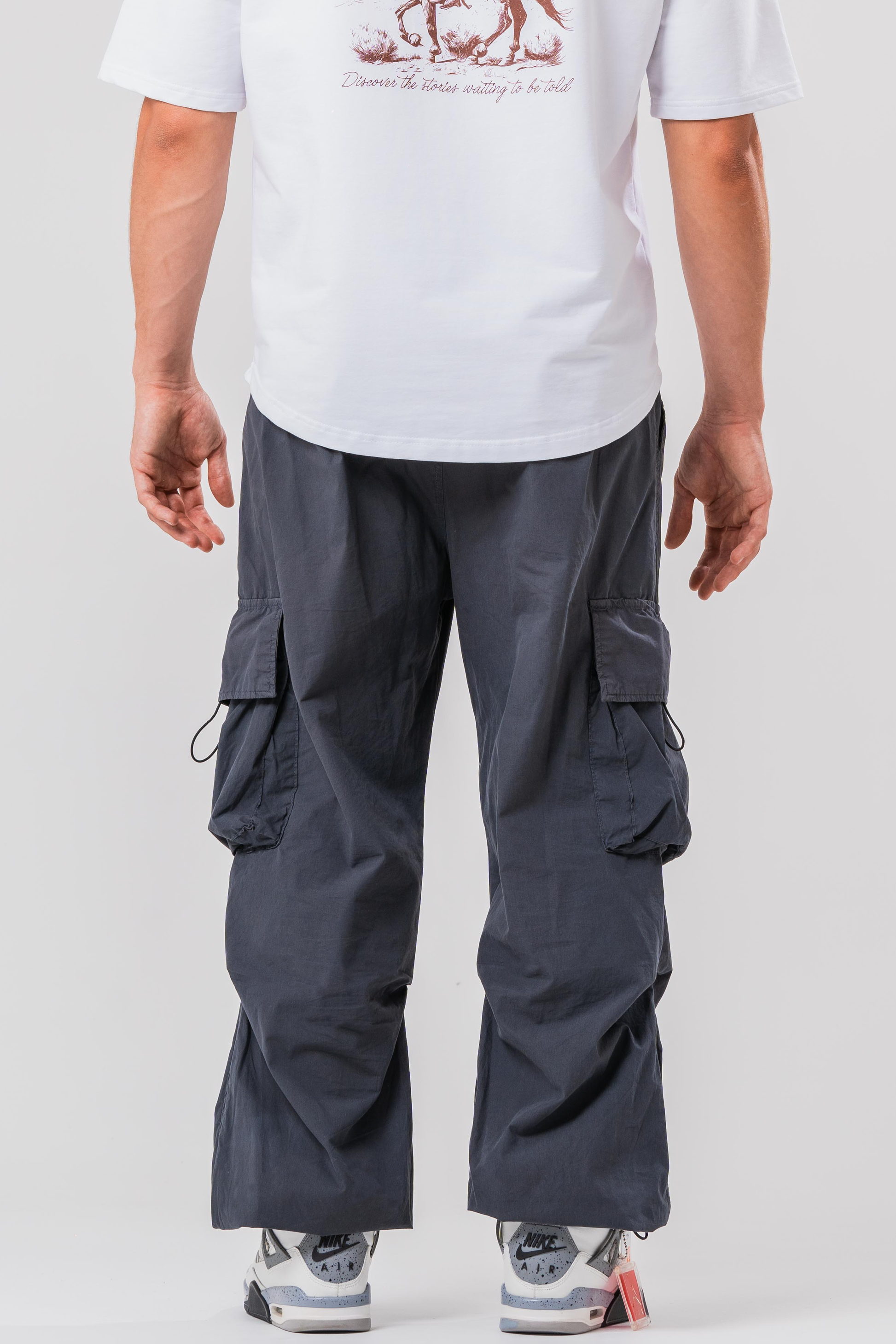 Back view of Male model wearing the Sonder Grey Oversized Cargo Pants and Sonder White Oversized Graphic Cowboy T-Shirt. In front of light grey background.