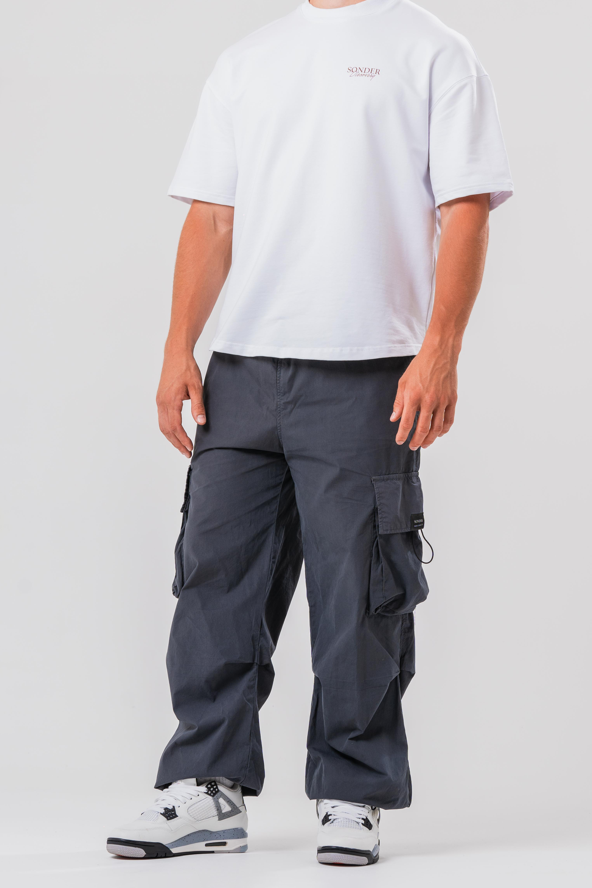 Side view of Male model wearing the Sonder Grey Oversized Cargo Pants and Sonder White Oversized Graphic Cowboy T-Shirt. In front of light grey background.
