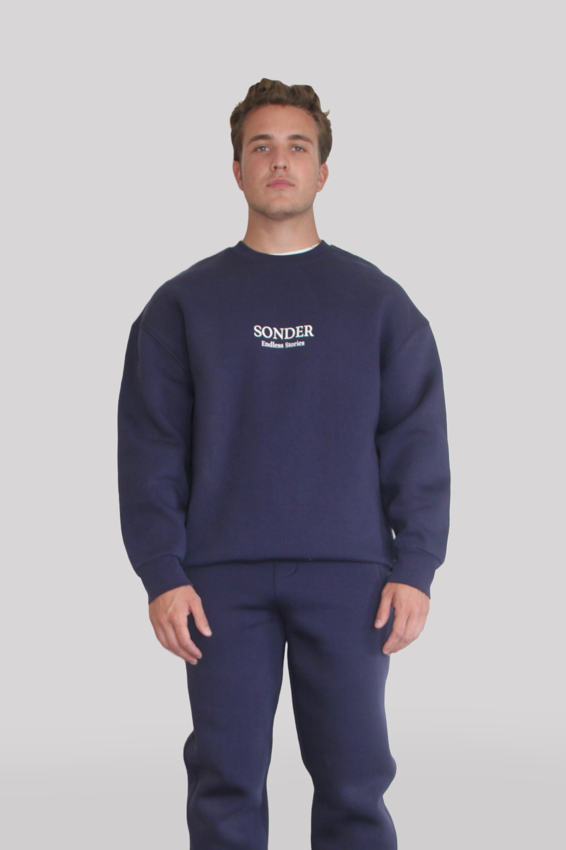 Male model wearing the Sonder Navy Signature Series Sweatshirt with SONDER branding paired with the Navy Signature Series Sweatpants. In front of a light grey background