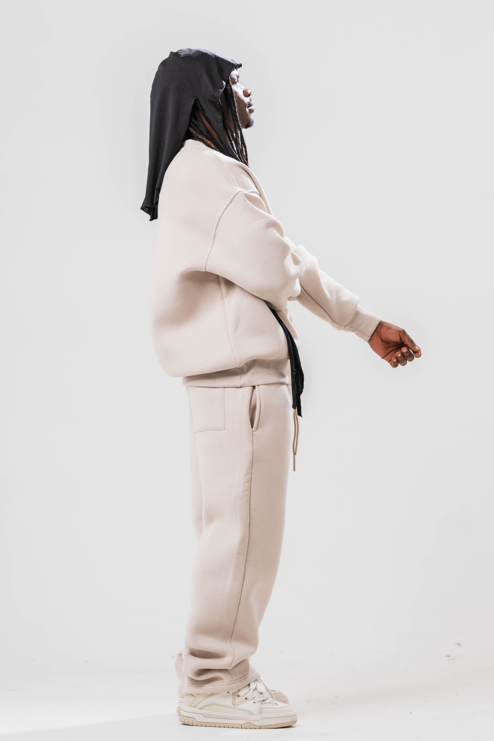 Side view of Male model wearing the Sonder Off-White Oversized sweatshirt with the oversized joggers. Standing in front of a light grey background.