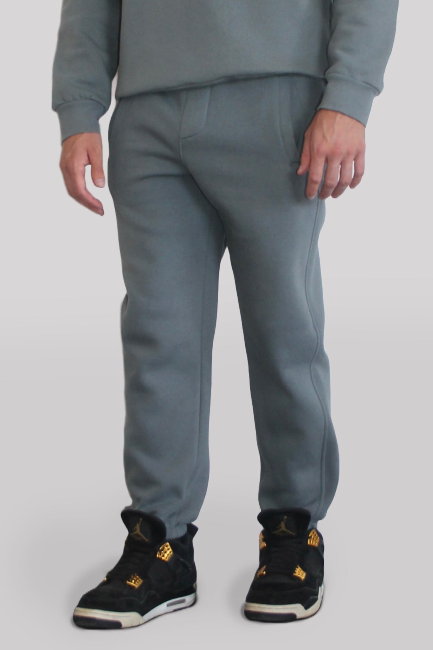 Side view of Male model wearing the Sonder Shadow Grey Signature Series Sweatpants paired with the Shadow Grey Signature Series Sweatshirt. In front of a light grey background.