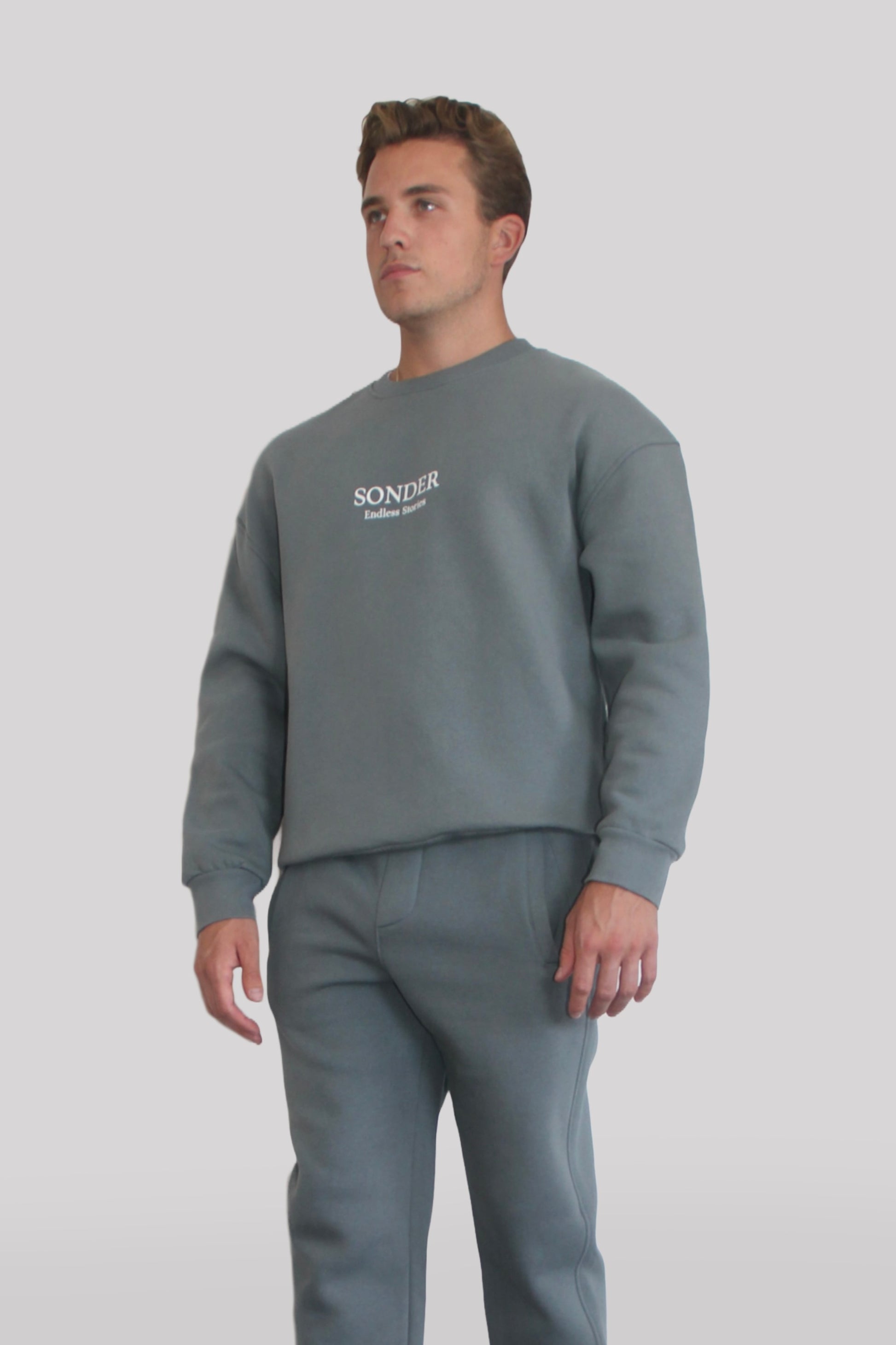 Side view of Male model wearing the Sonder Shadow Grey Signature Series Sweatshirt with SONDER branding paired with the Shadow Grey Signature Series Sweatpants. In front of a light grey background