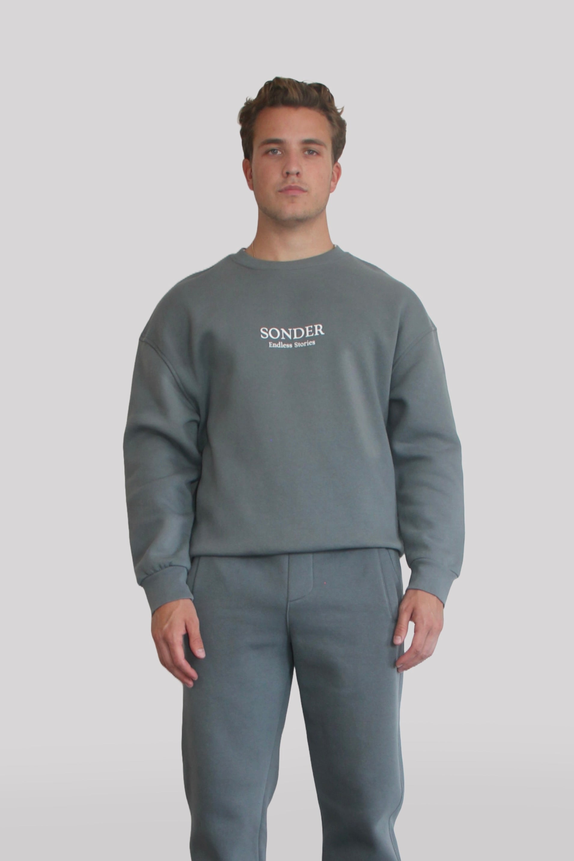 Male model wearing the Sonder Shadow Grey Signature Series Sweatshirt with SONDER branding paired with the Shadow Grey Signature Series Sweatpants. In front of a light grey background