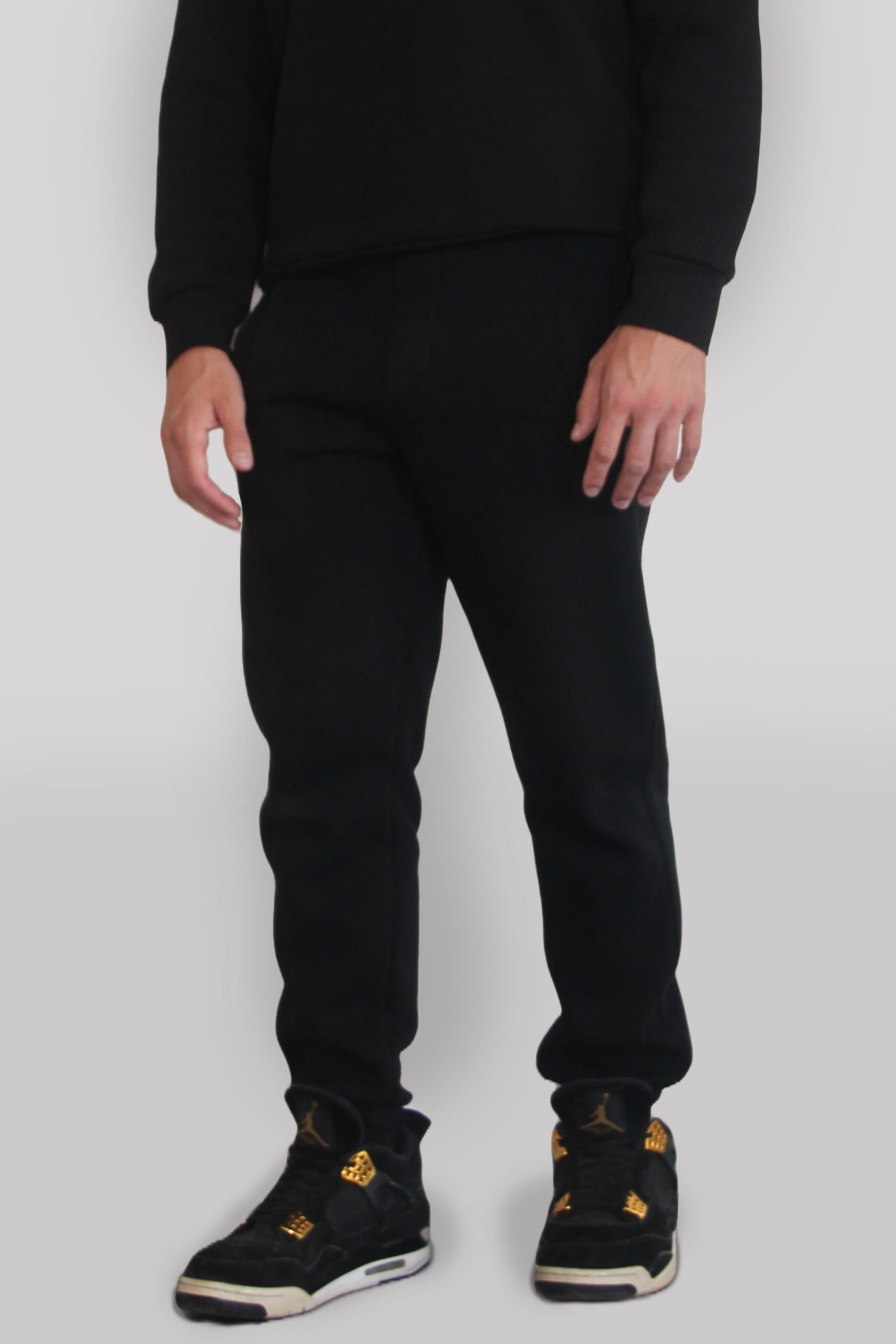 Side view of Male model wearing the Sonder black Signature Series Sweatpants paired with the Black Signature Series Sweatshirt. In front of a light grey background
