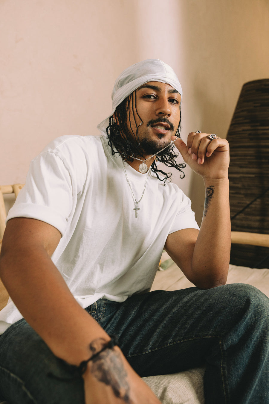Man wearing a white t-shirt and durag sitting indoors with a neutral background